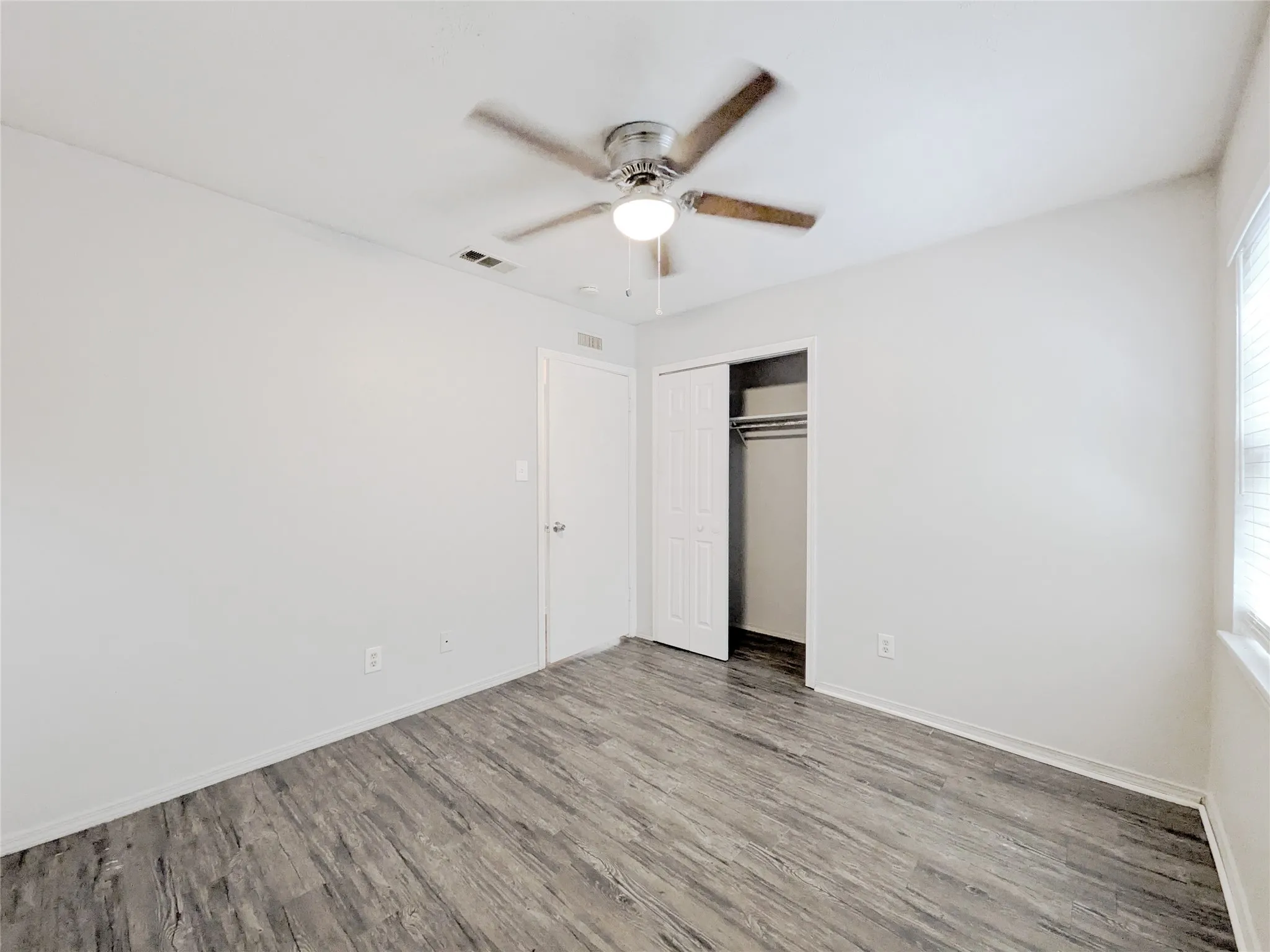 Wood-finish flooring, ceiling fan with light fixture, window with blinds, and a built-in closet with sliding doors