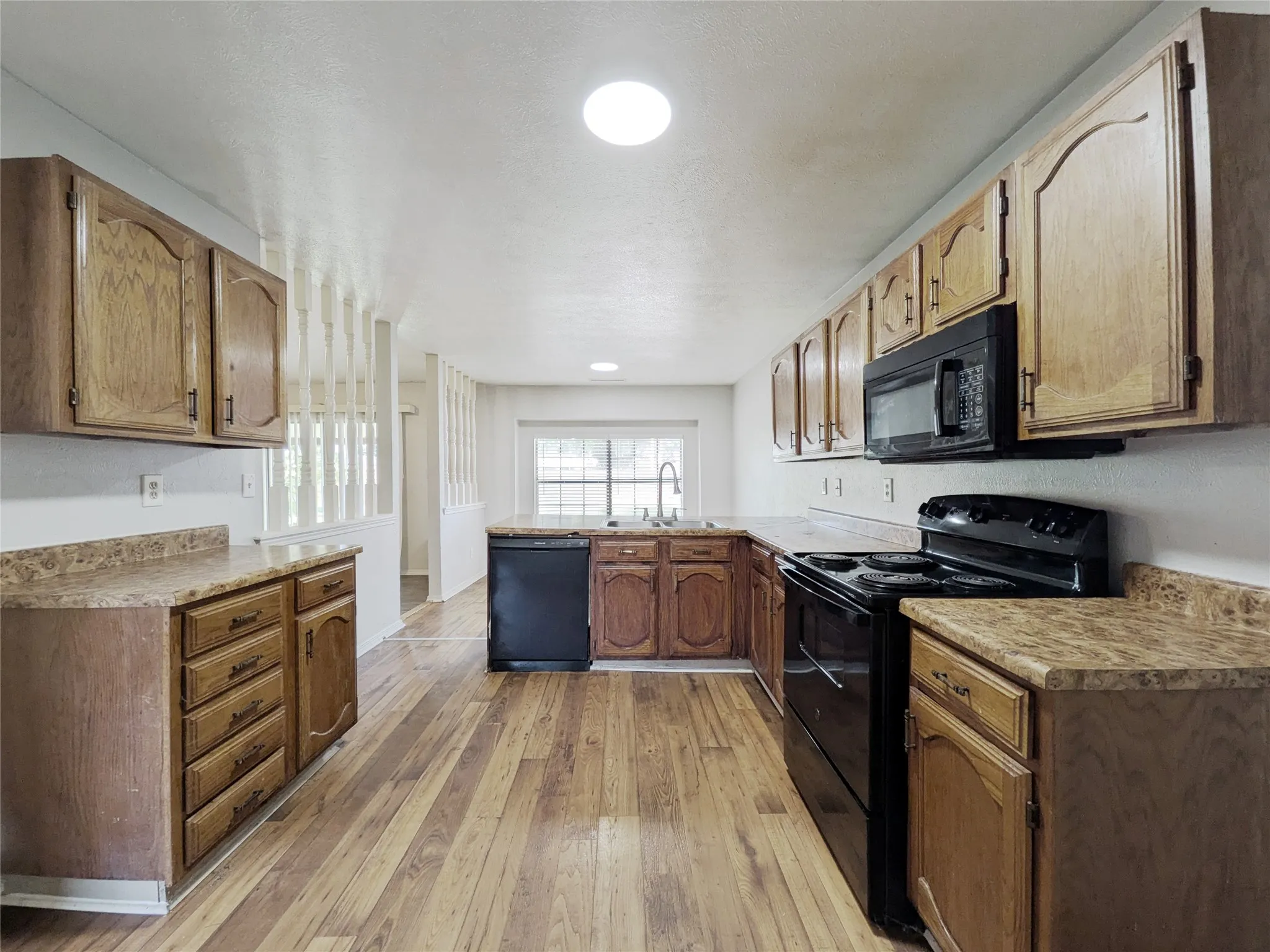 Kitchen featuring wood-finish flooring, wood cabinetry, dark countertops, and black appliances