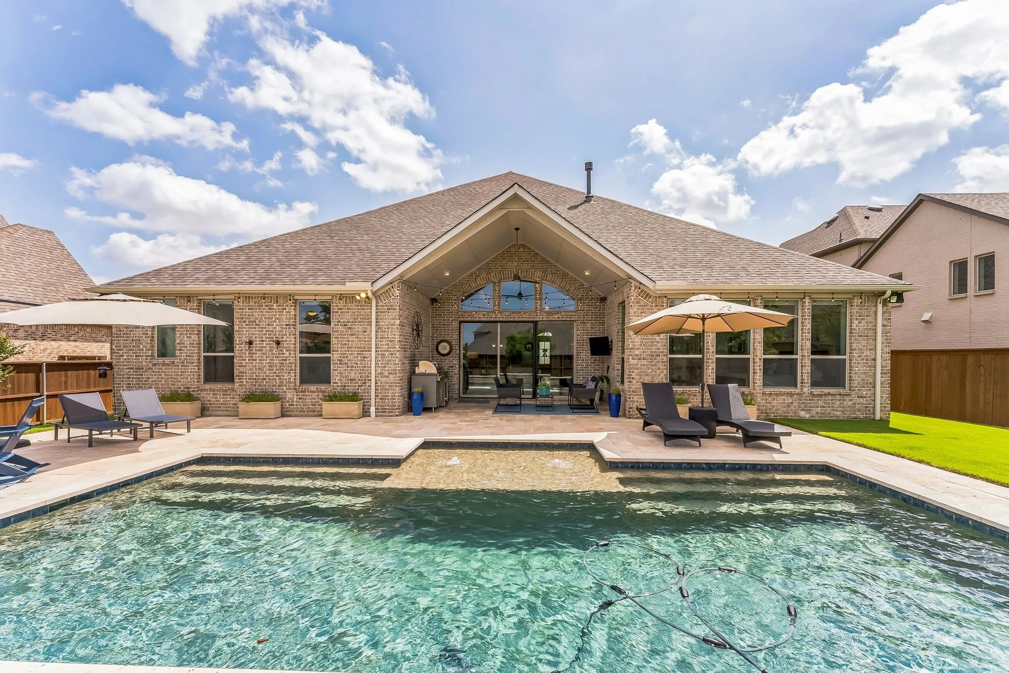 Brick exterior with a gabled roofline, outdoor swimming pool, integrated spa, and an expansive paved patio