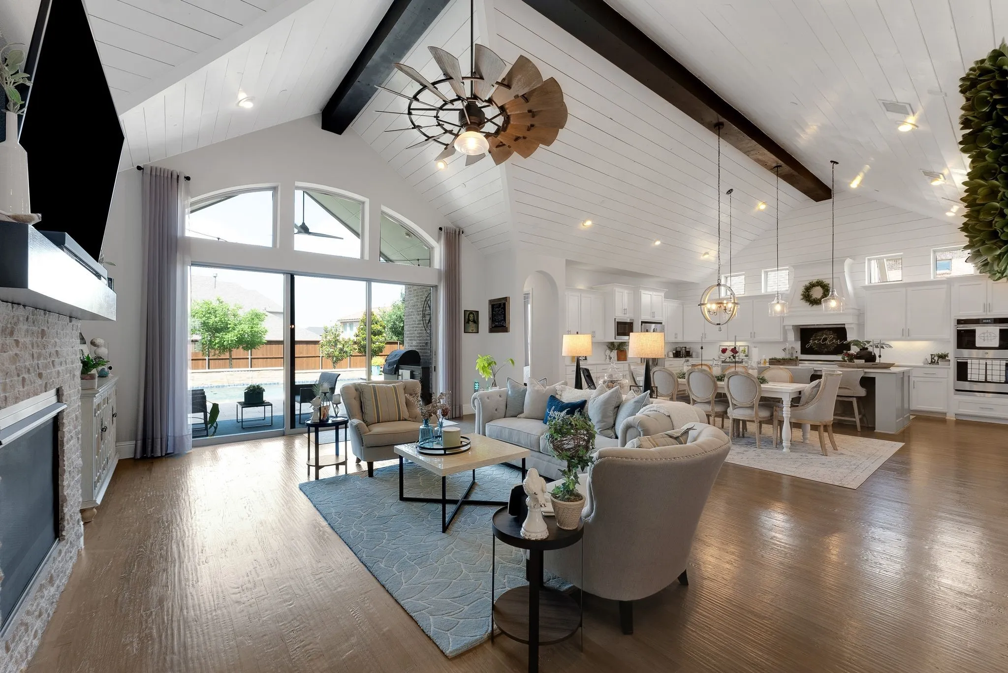 Vaulted plank ceiling with exposed beams, hardwood flooring, fireplace with stone surround, large sliding glass doors, built-in kitchen cabinetry with integrated appliances