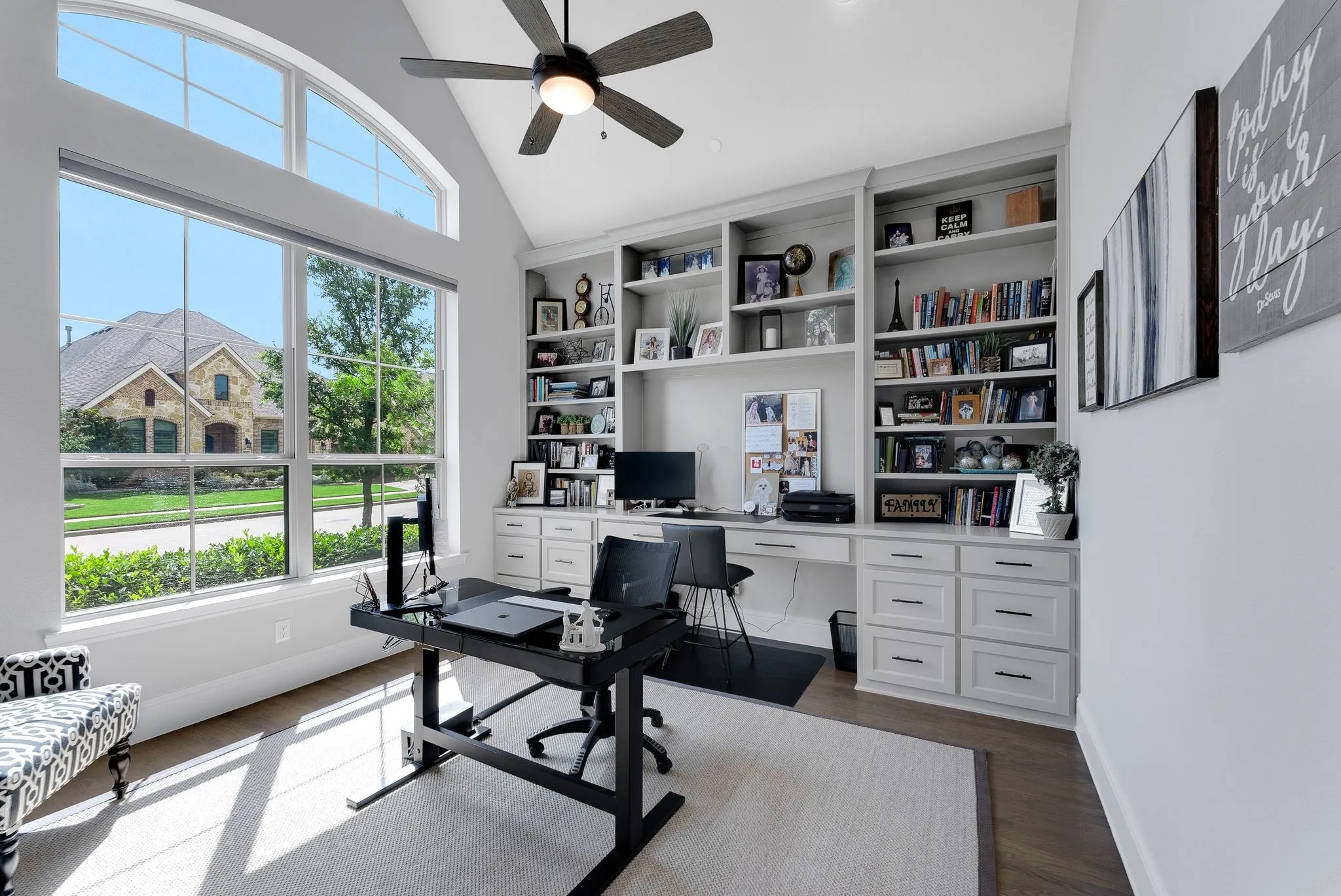 Cathedral ceiling with an arched transom window, large picture windows, built-in shelving with integrated desk, wood-finish flooring, and a ceiling fan