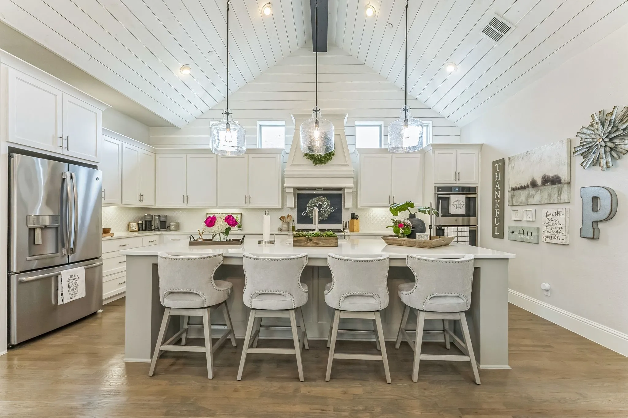 Vaulted shiplap ceiling, wood-finish flooring, white cabinetry, integrated stainless steel appliances, and a central island with countertop seating