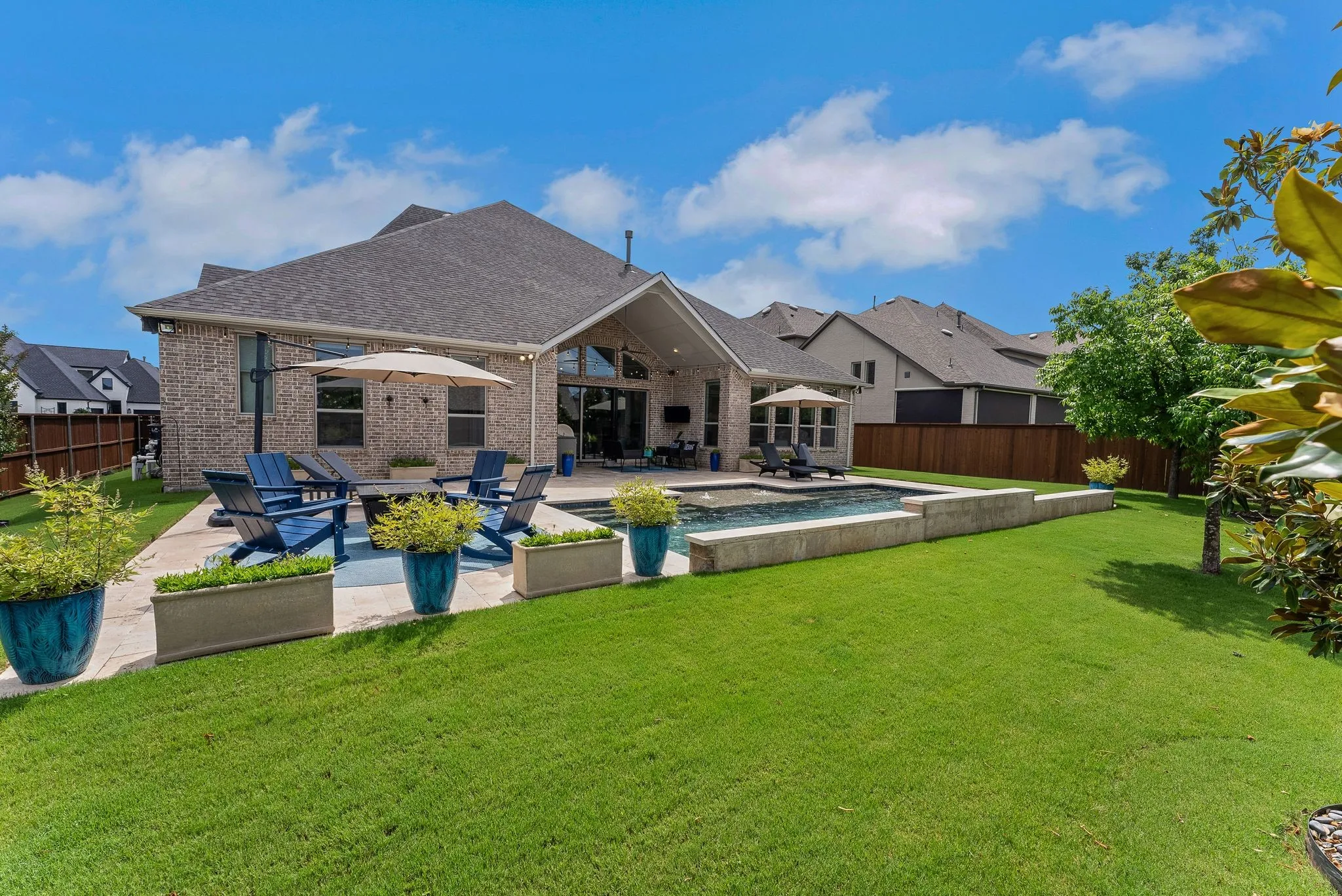 Expansive backyard featuring a rectangular swimming pool, concrete patio, brick exterior, and a gable roofline