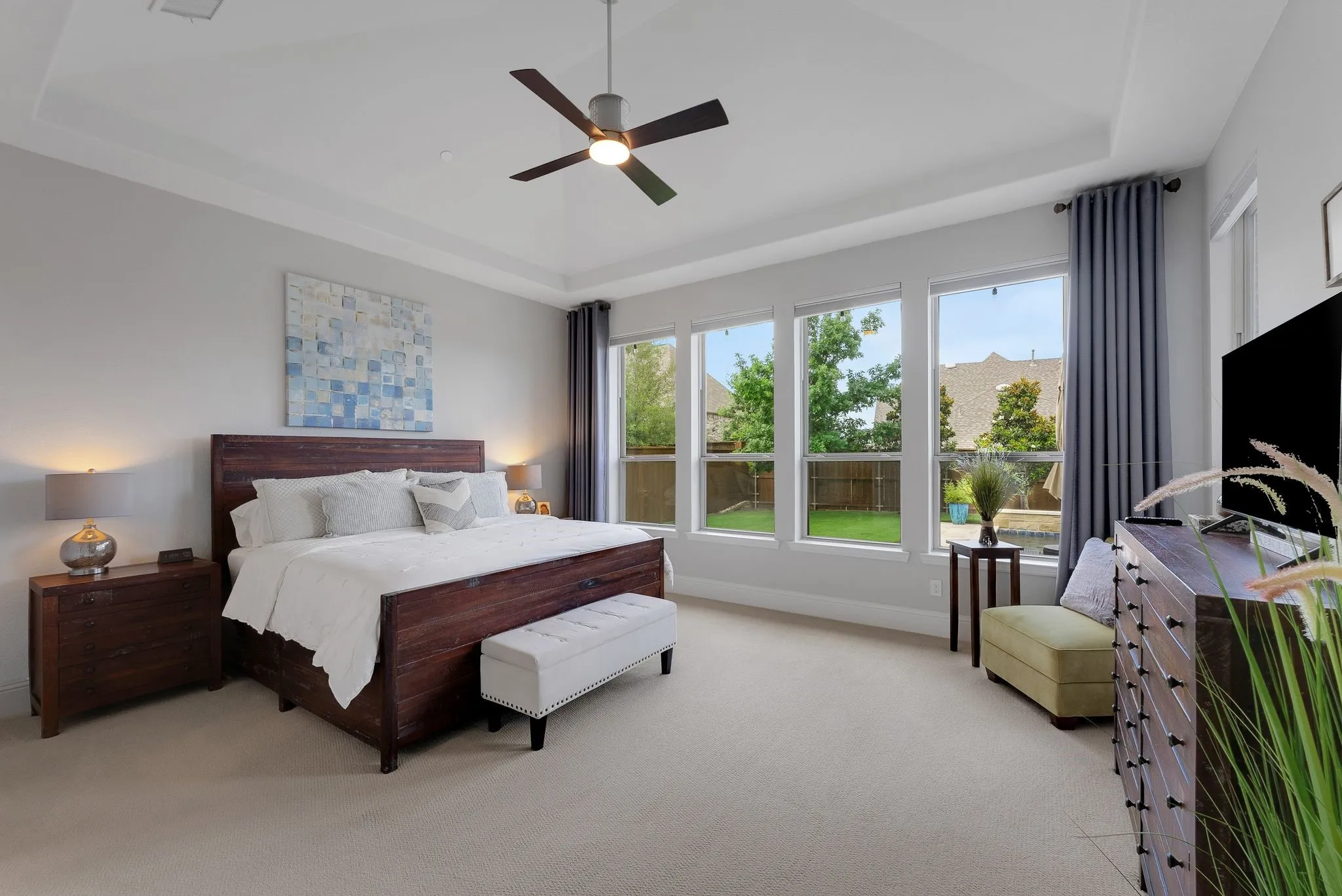 Tray ceiling, ceiling fan, expansive windows, light gray walls, and carpeting