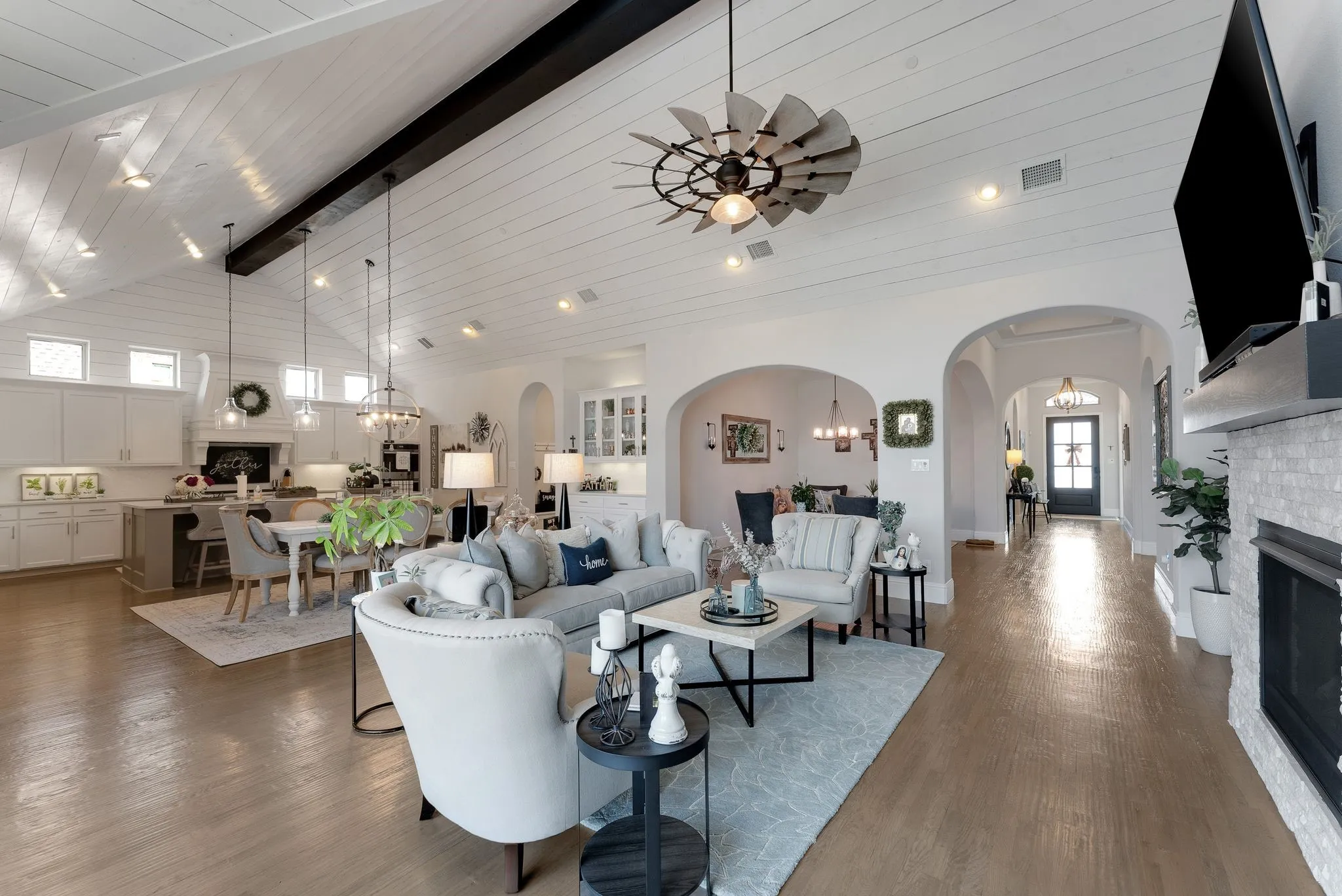 Vaulted shiplap ceiling with exposed beam, arched doorways, light wood-finish flooring, fireplace with white tile surround, and open-concept design