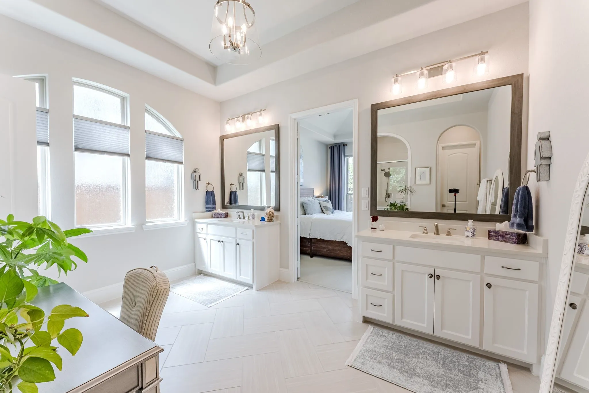 Dual vanity sinks, individual framed mirrors, vanity lighting, white cabinetry, and a tray ceiling