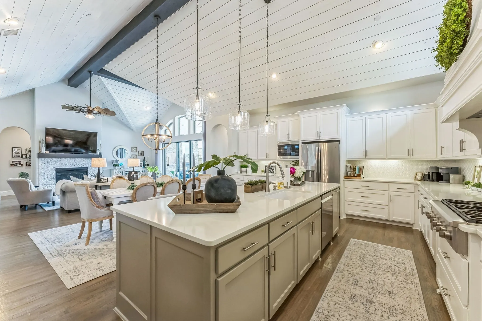 Kitchen featuring an expansive island with a light-toned countertop, white cabinetry with under-cabinet lighting, stainless steel appliances, and wood-finish flooring