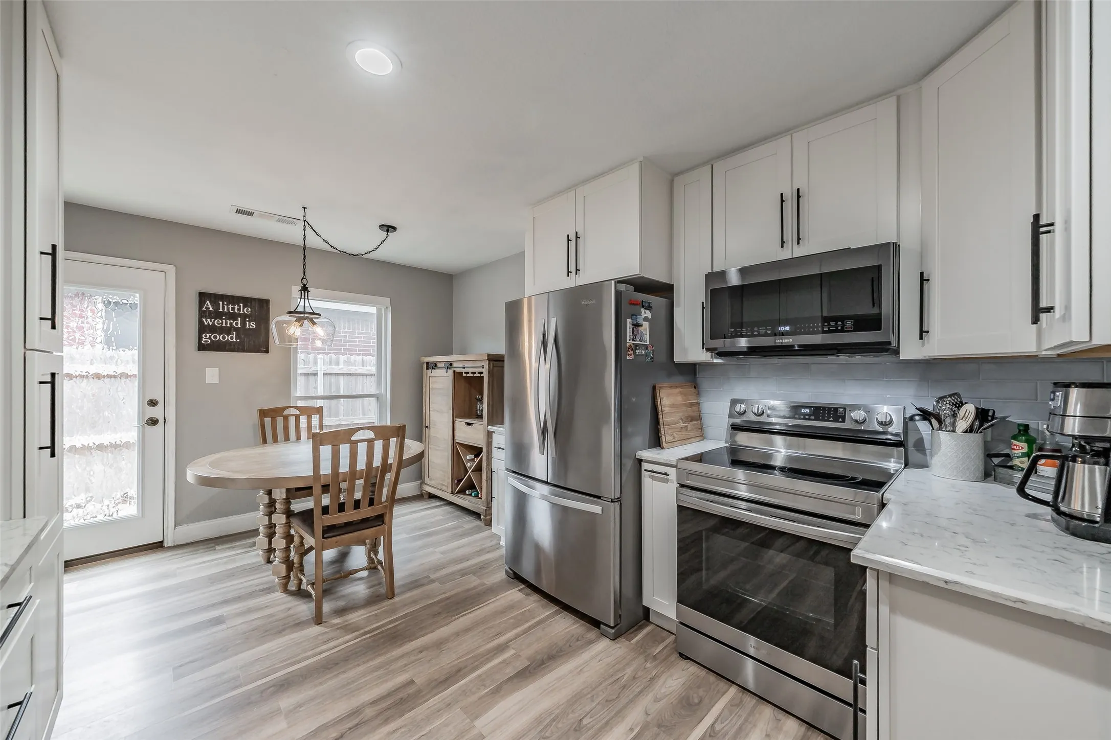 Kitchen featuring white cabinetry with dark hardware, stainless steel appliances, light-toned wood-finish flooring, and light countertops