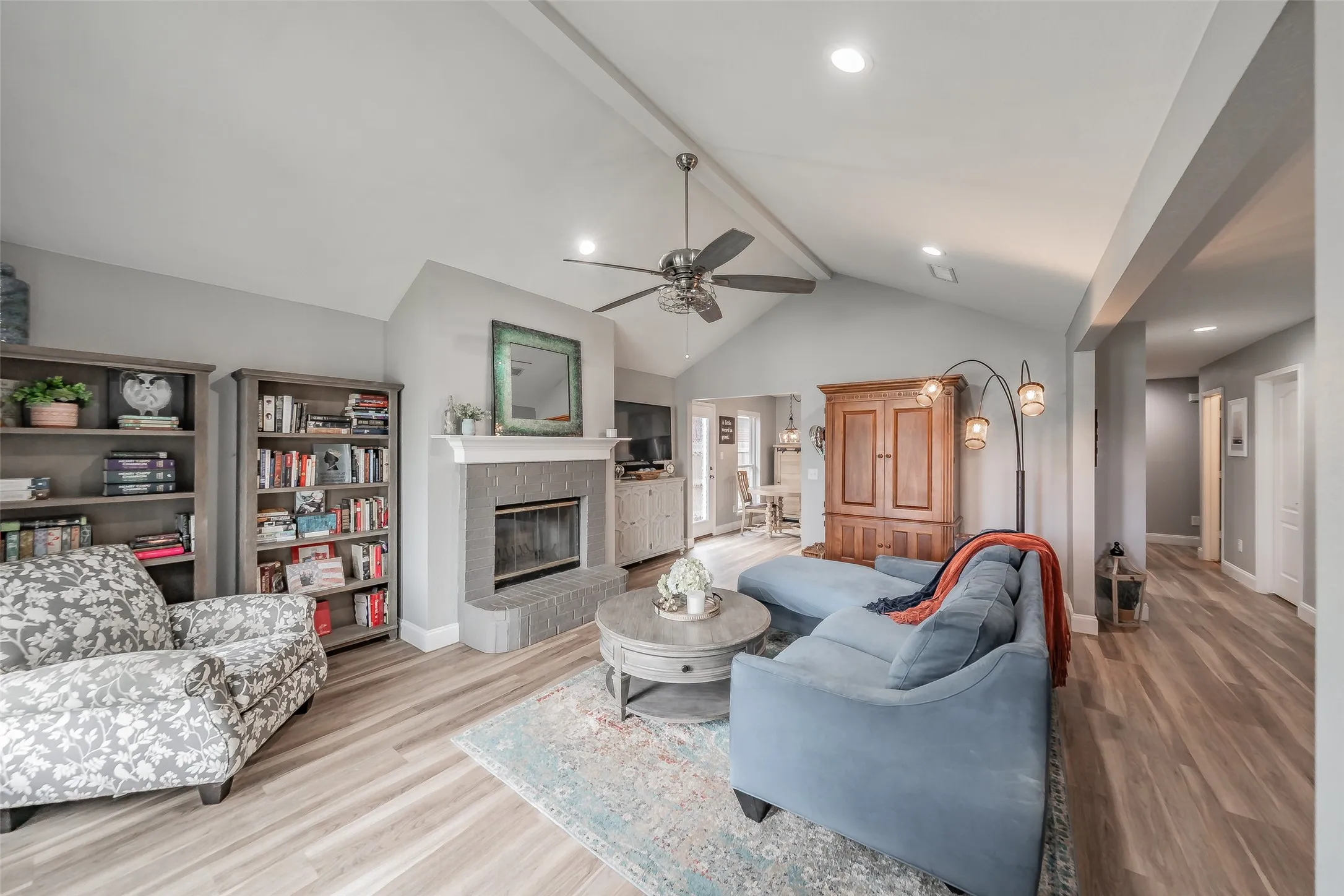 Vaulted ceiling with exposed beam, recessed lighting, ceiling fan, wood-finish flooring, and a fireplace with a mantel