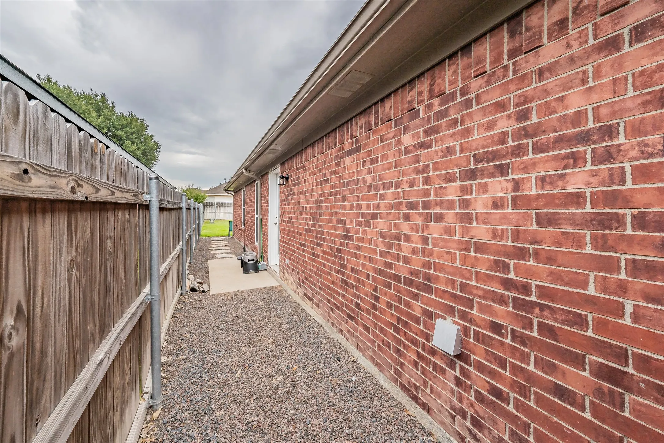 Red brick exterior, wood privacy fence, gravel pathway, concrete stepping stones, exterior door with light fixture