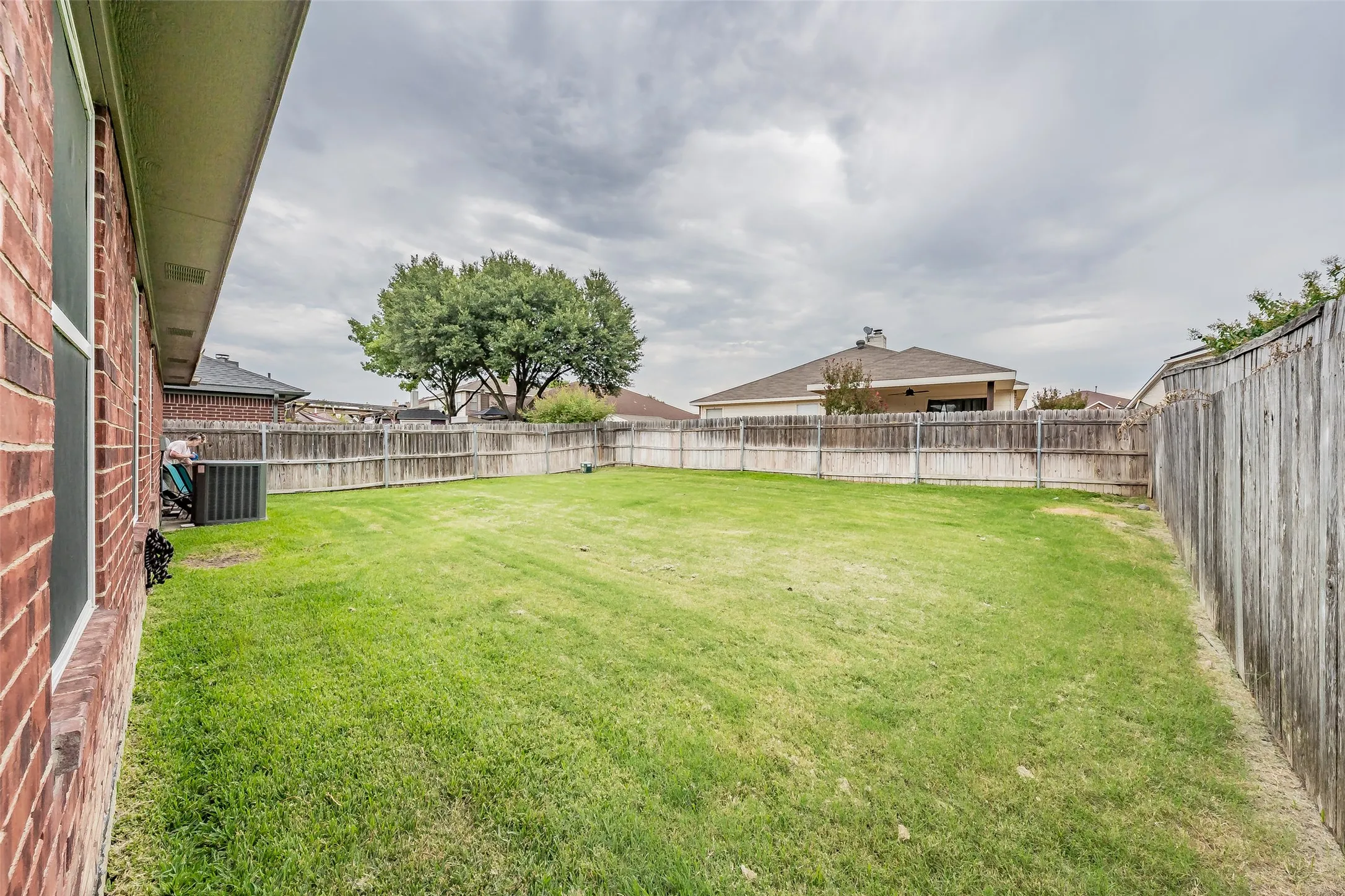 Expansive backyard featuring a manicured lawn, full wood privacy fencing, and mature trees