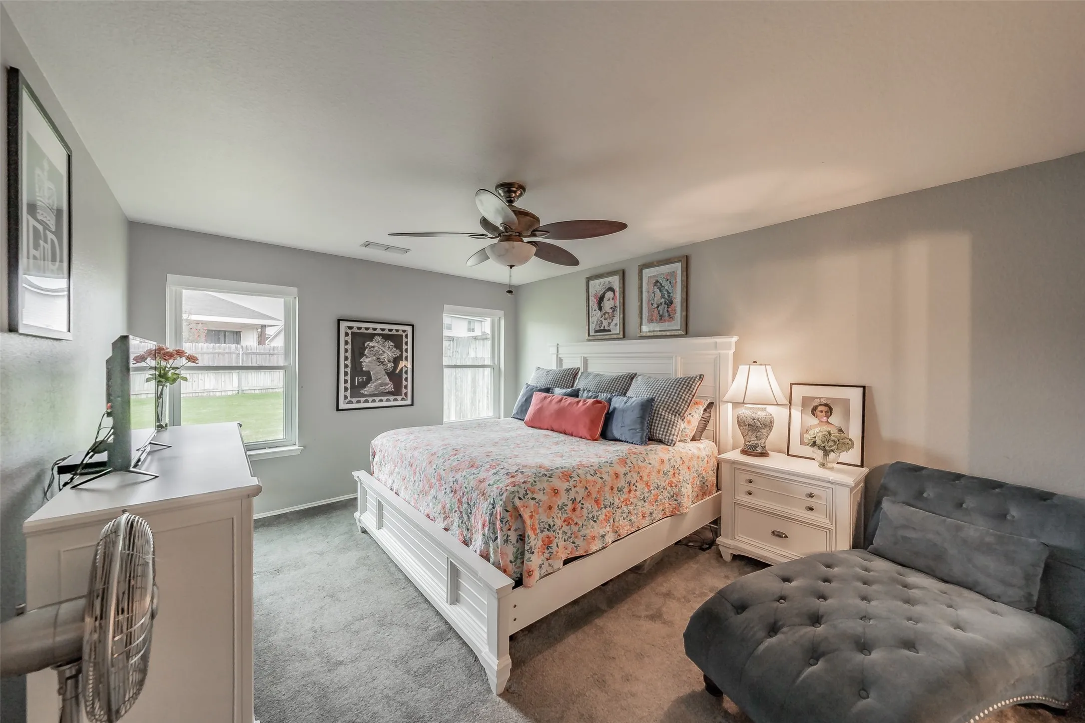 Sloped ceiling with an integrated ceiling fan, light gray wall paint, and two windows providing outdoor scenery