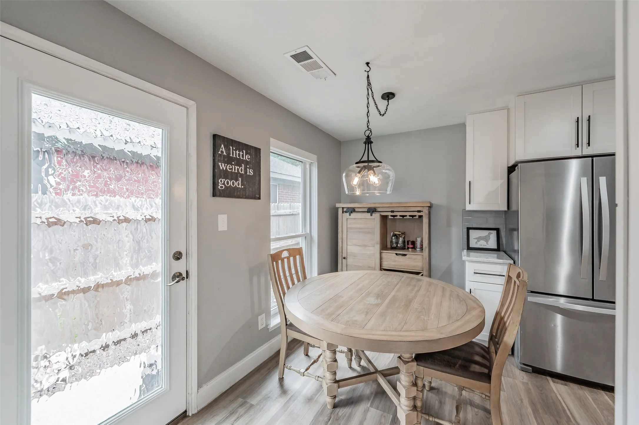 Wood-finish flooring, white cabinetry with dark hardware, and a stainless steel refrigerator