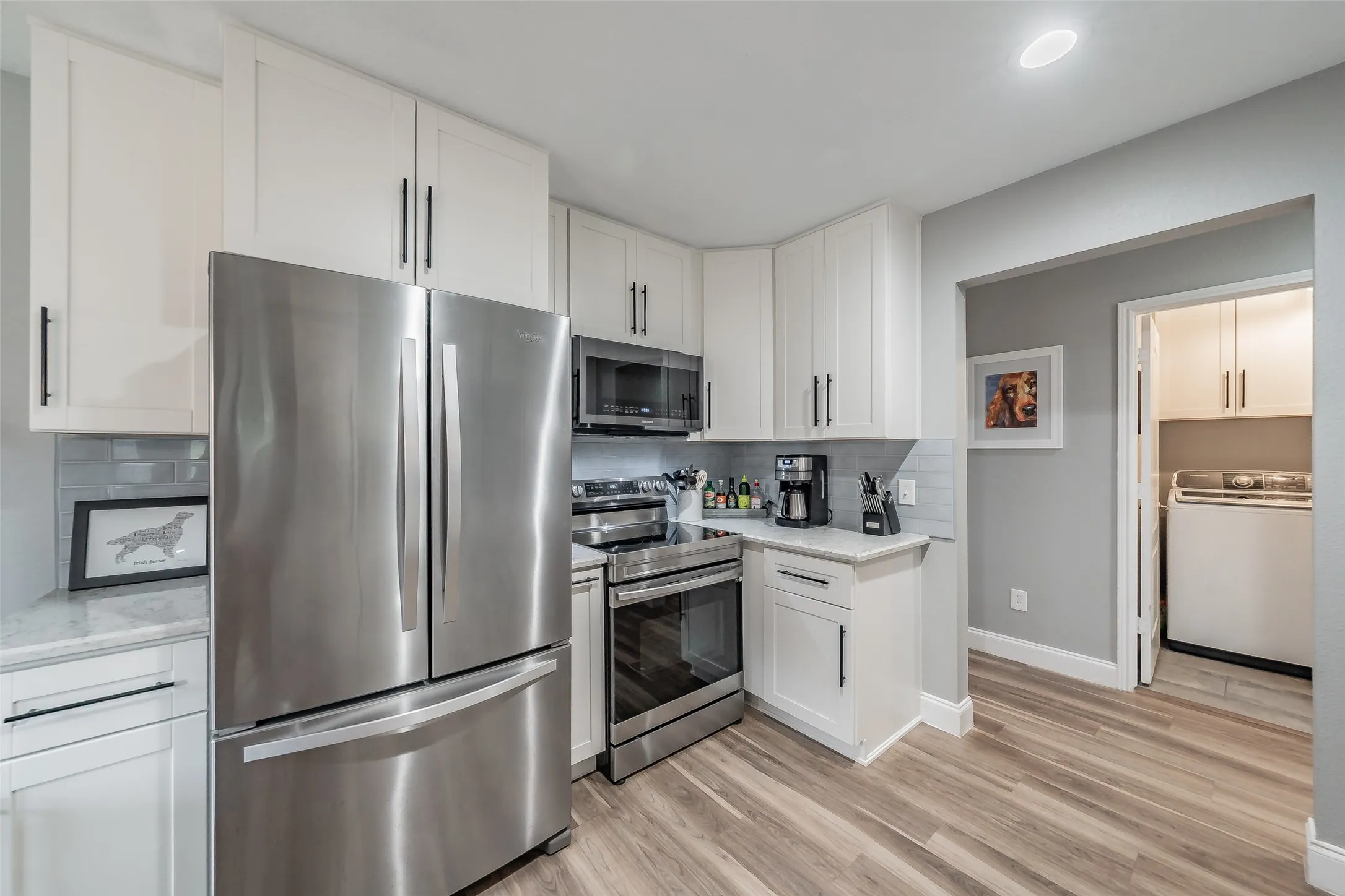 Modern kitchen featuring white shaker-style cabinetry, stainless steel appliances, light-toned countertops, and wood-finish flooring