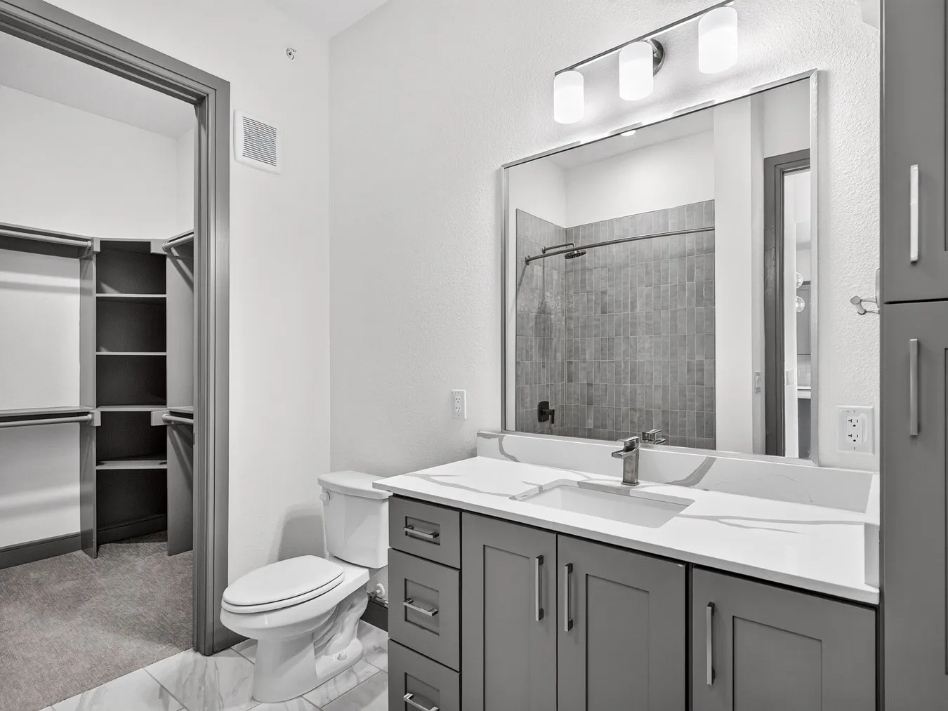 Vanity with integrated sink and chrome faucet, large mirrored wall, tile flooring, and a walk-in closet with built-in shelving