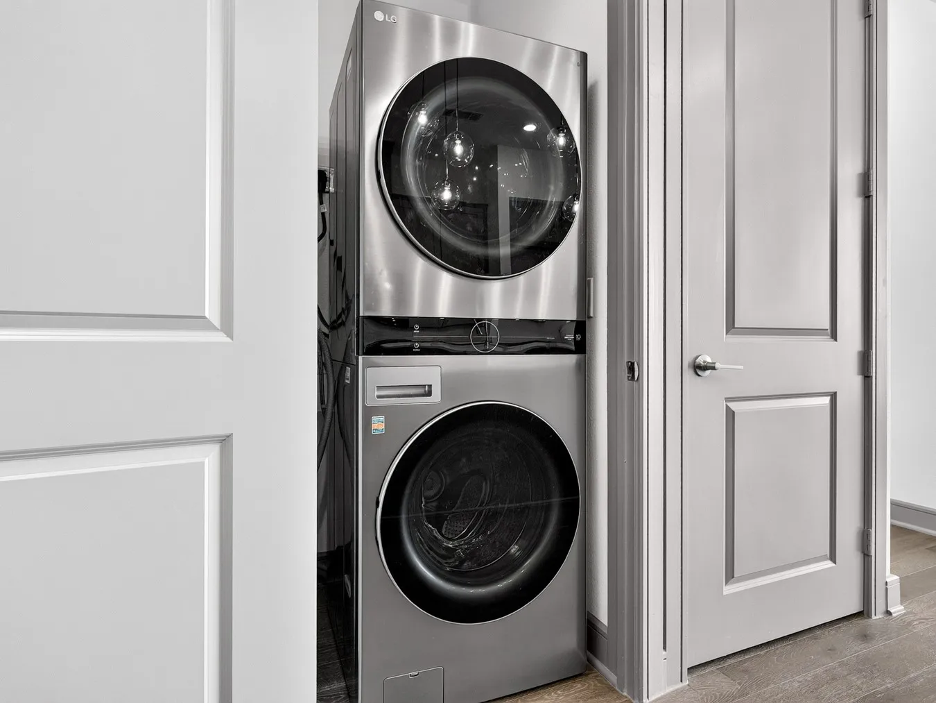 Stackable stainless steel washer and dryer unit, paneled doors with contemporary hardware, and wood-finish flooring