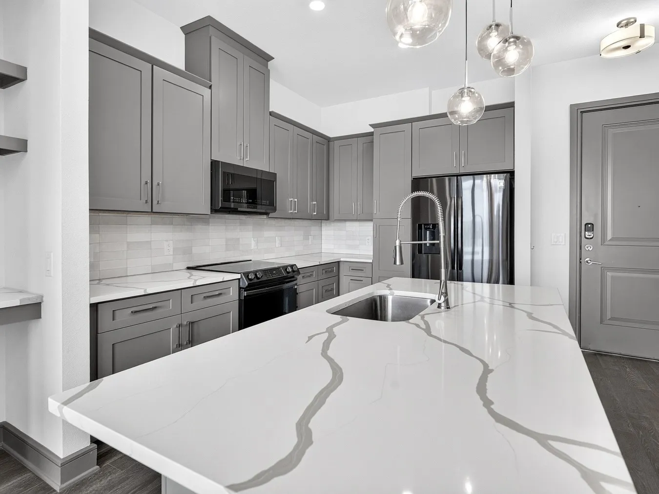 Kitchen featuring a large island with an integrated sink, grey cabinetry, stainless steel appliances, and a tiled backsplash