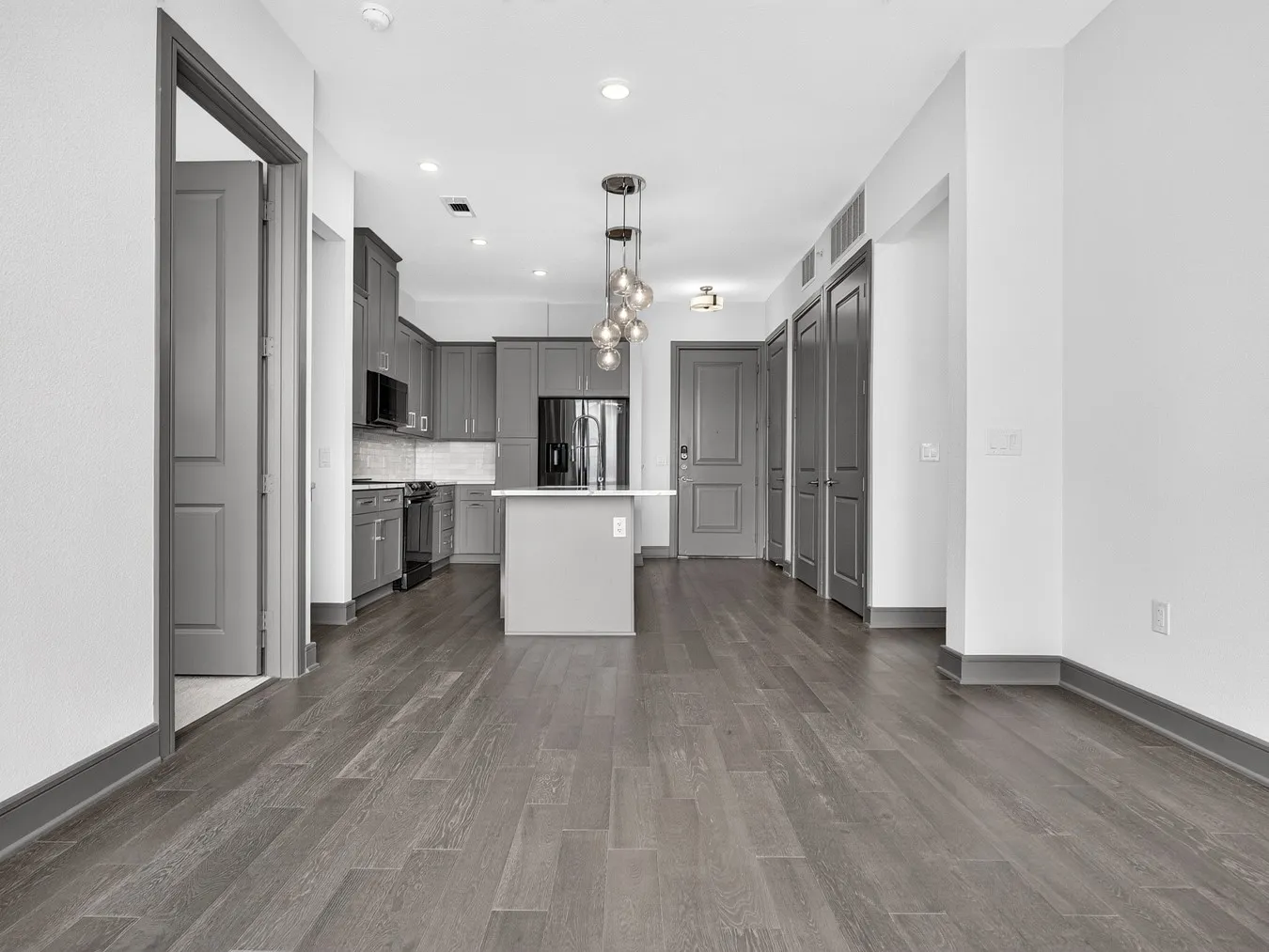 Expansive wood-finish flooring throughout, modern kitchen with gray cabinetry, kitchen island with countertop, and recessed lighting