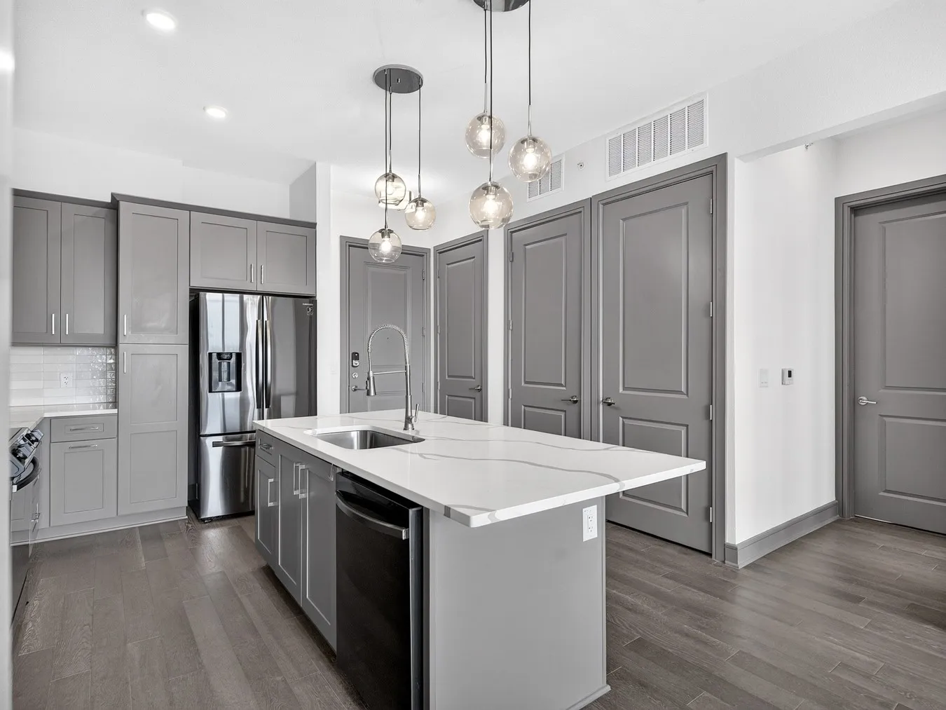 Kitchen featuring a center island with a sink, stainless steel appliances, wood-finish flooring, and pendant lighting
