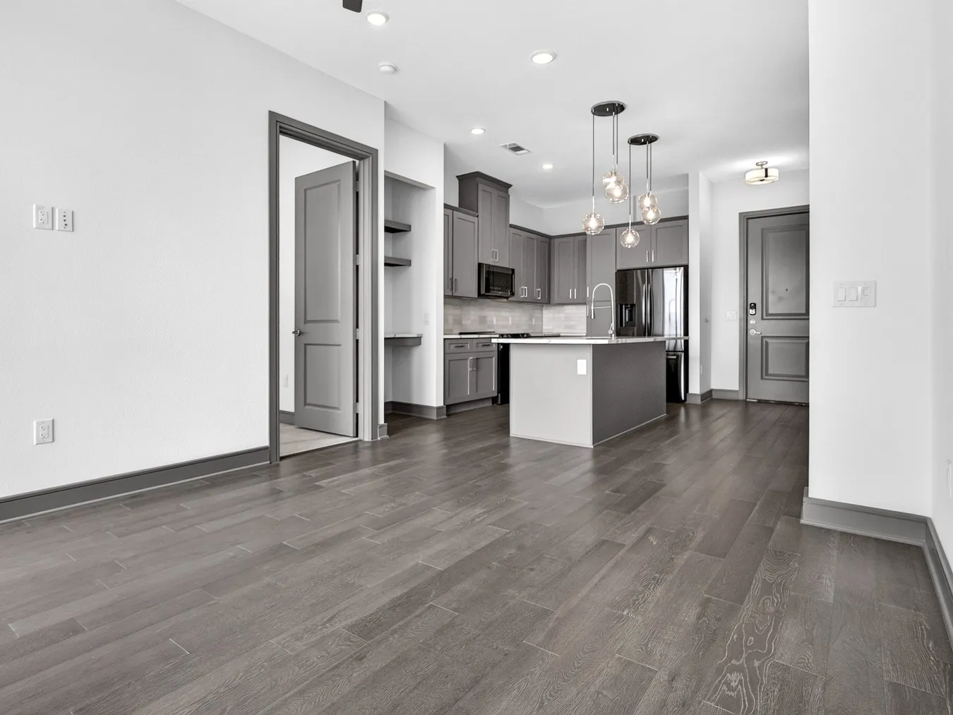 Wood-finish flooring throughout, kitchen with gray cabinetry, central island, and modern pendant lighting