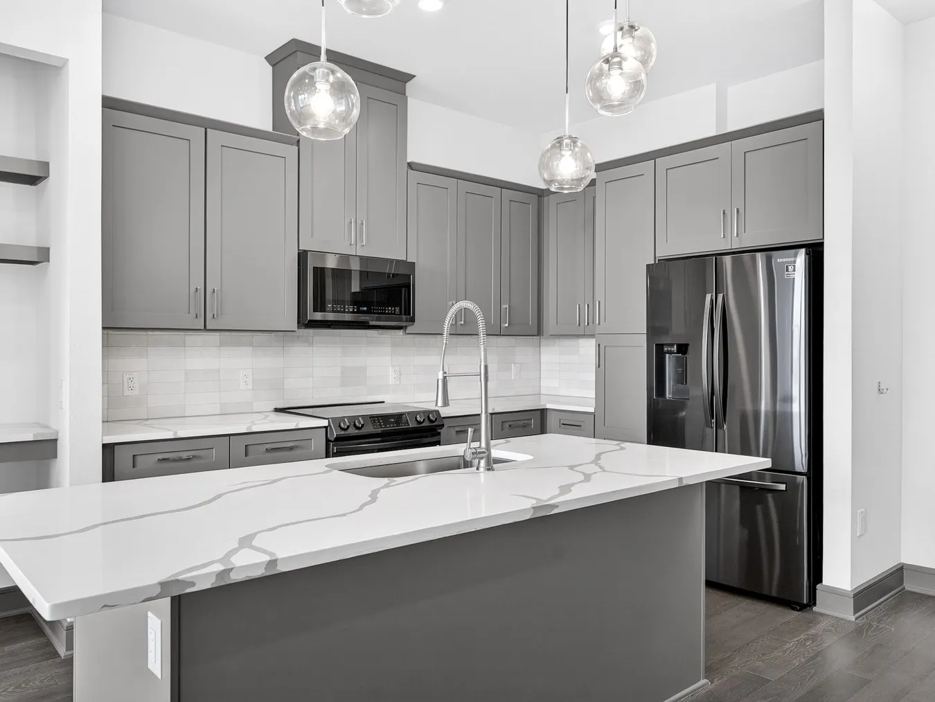 Kitchen featuring gray cabinetry, white countertops with veining, stainless steel appliances, a white tile backsplash, and wood-finish flooring