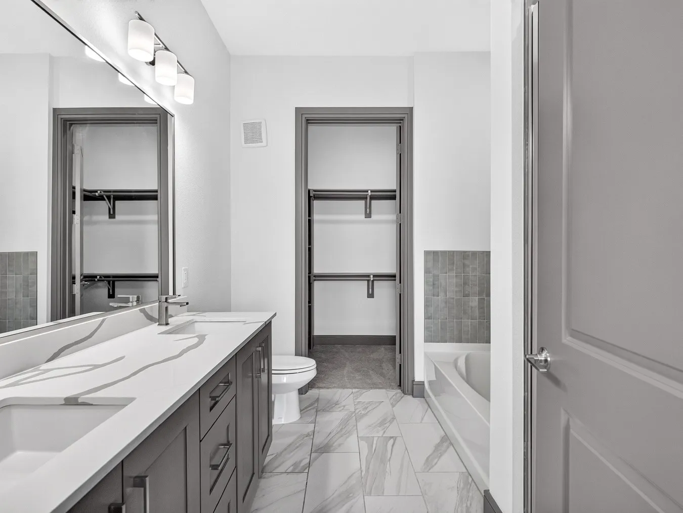 Dual sink vanity with quartz-finish countertop and contemporary fixtures, integrated soaking tub with subway tile surround, and tile flooring