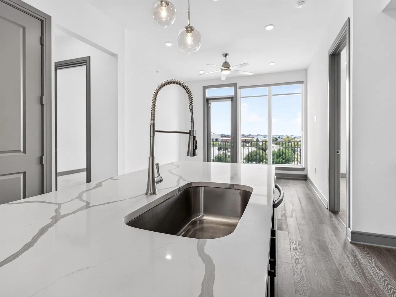 Integrated stainless steel sink with a pull-down faucet, large countertop space, wood-finish flooring, ceiling fan, and prominent windows