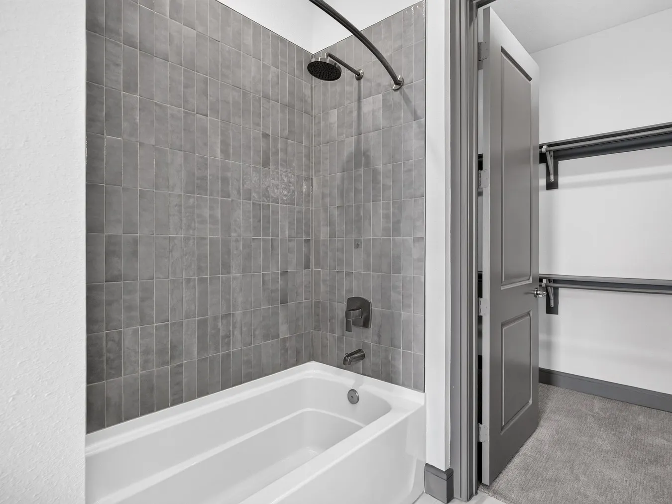 Bathtub with subway tile surround, matte black shower fixtures, and an adjacent closet with built-in shelving