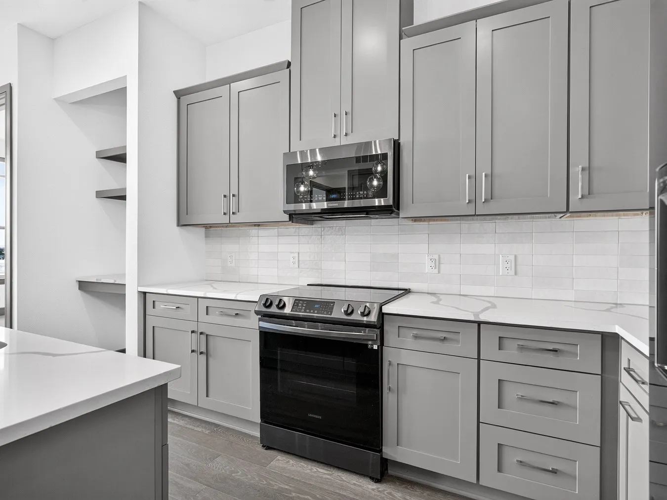 Sleek kitchen with gray shaker-style cabinetry, stainless steel microwave, and a black electric range