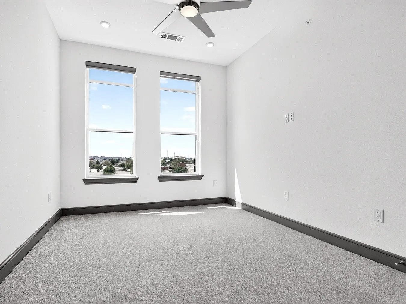 Recessed lighting, two large windows, a ceiling fan, and light gray carpeting