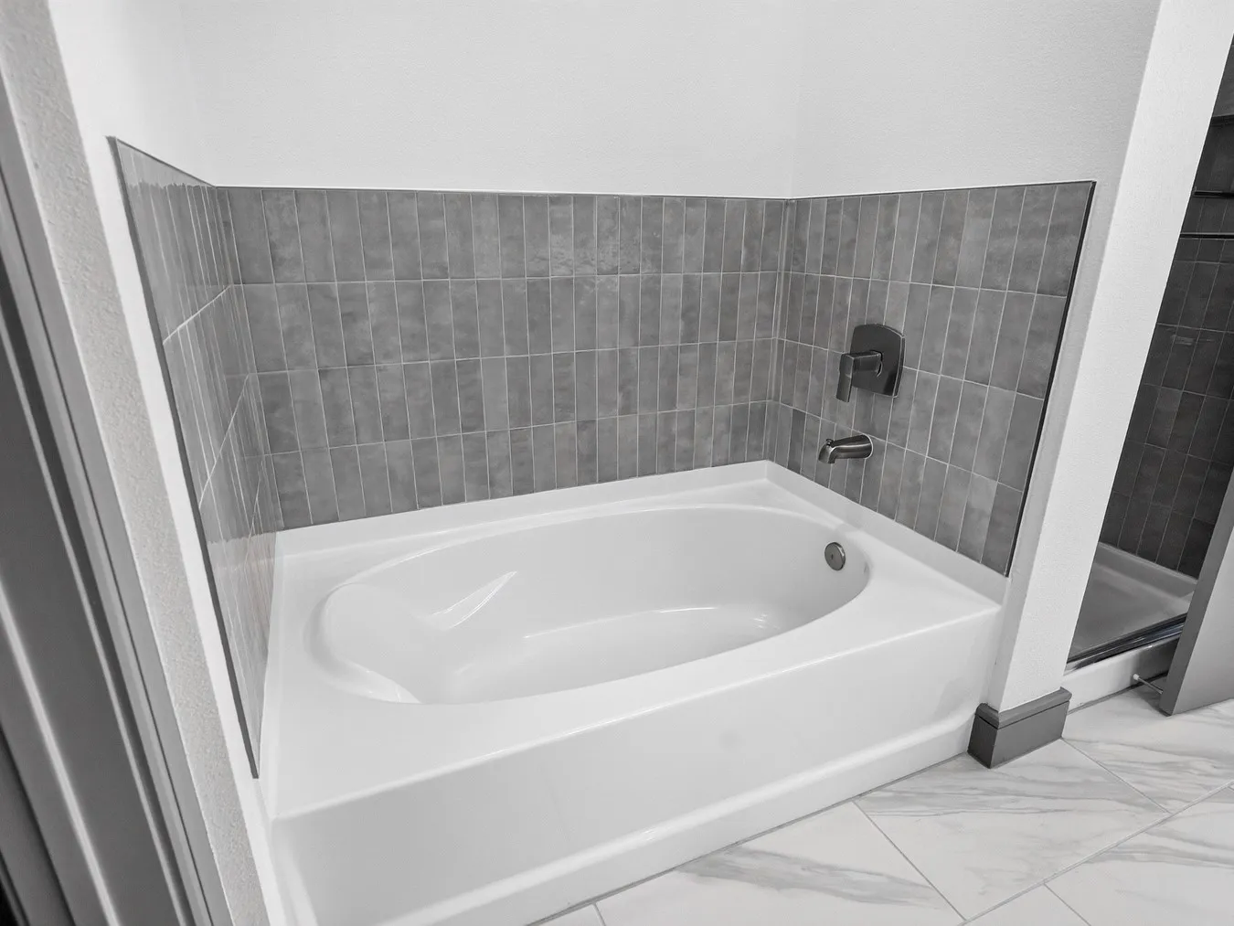 Built-in soaking tub with gray subway tile surround and chrome fixtures