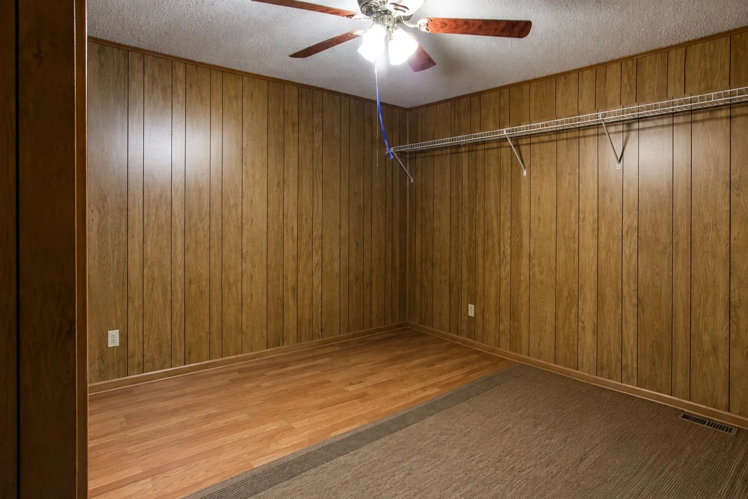 Ceiling fan with light fixture, wood-finish wall paneling, mixed flooring with wood-finish and carpet, wire shelving system