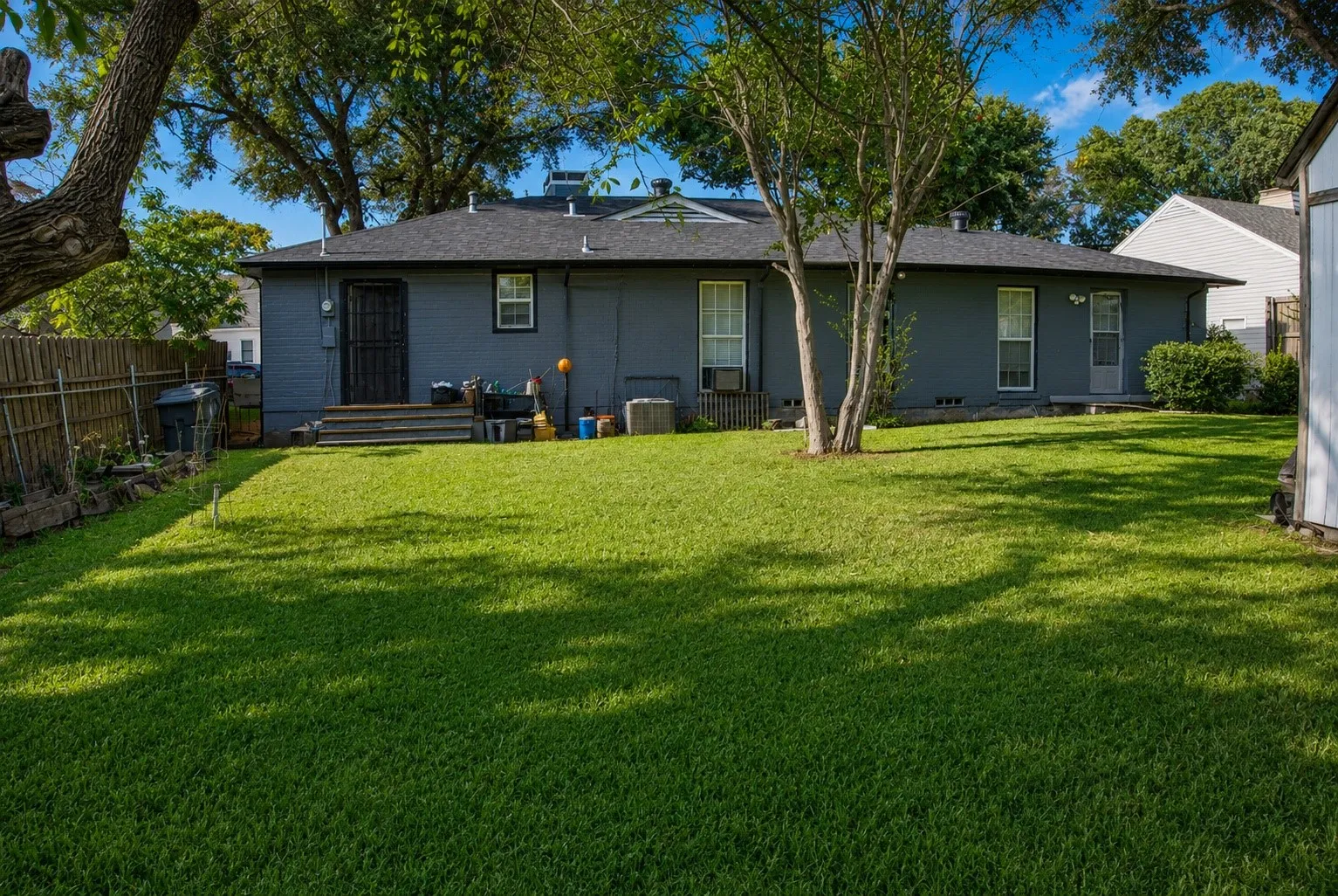 Expansive backyard featuring a manicured lawn, established trees, privacy fencing, and a utility shed