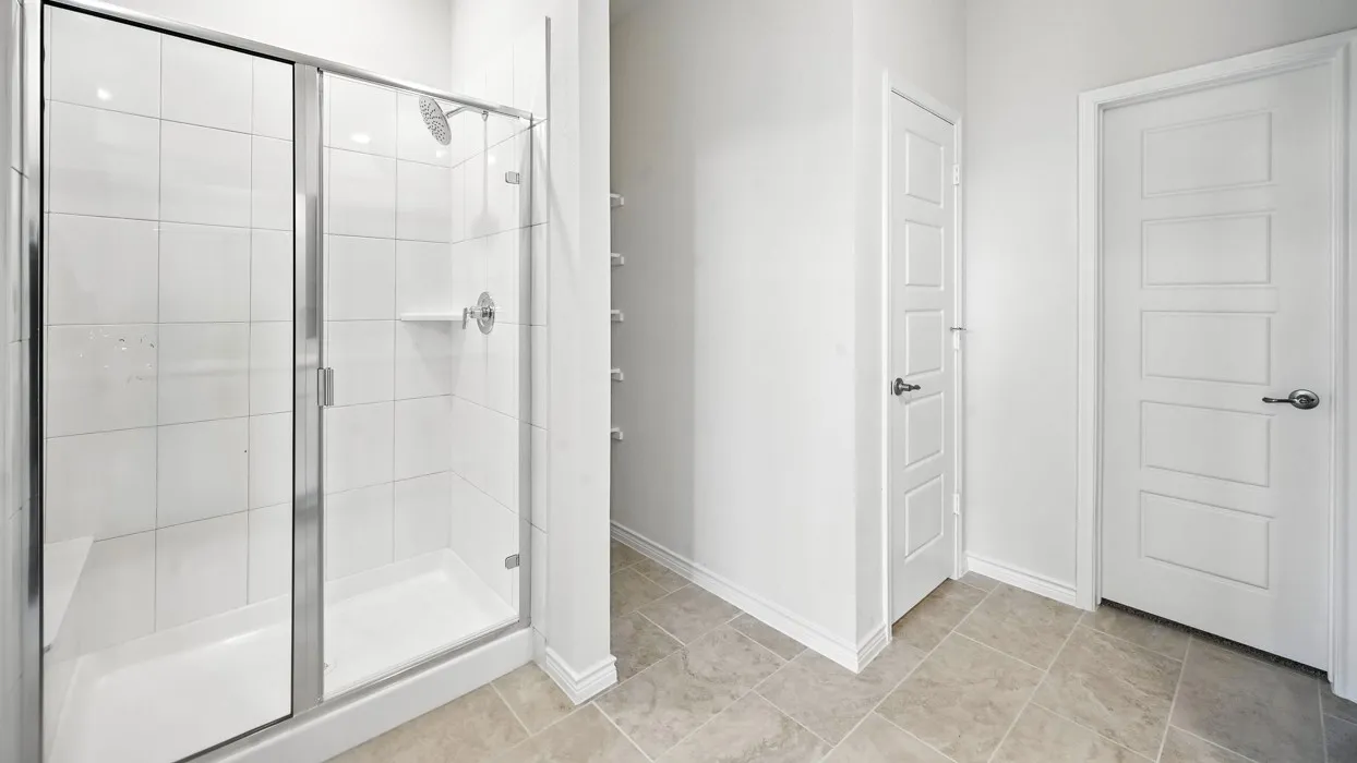 Primary Bathroom featuring a frameless glass-enclosed shower with subway tile surround, ceramic tile flooring, and dual entry doors leading to the vanity and bedroom areas