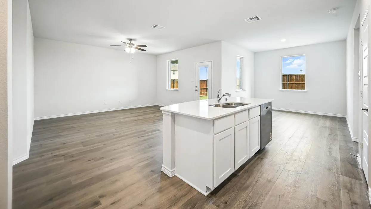 Open-concept kitchen and living area featuring wood-finish flooring throughout, a large center island with white cabinetry and stainless steel appliances, quartz countertops, recessed lighting, and abundant natural light from multiple windows