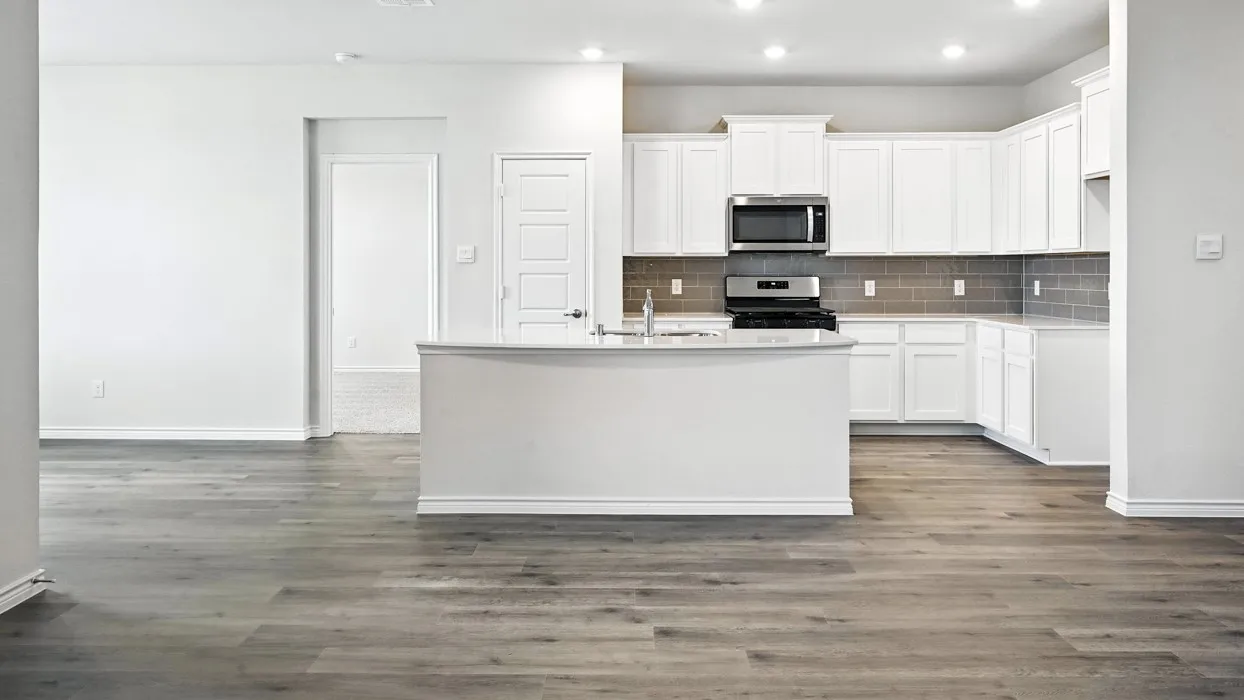 Wood-finish flooring throughout, white cabinetry, stainless steel microwave, and gray subway tile backsplash