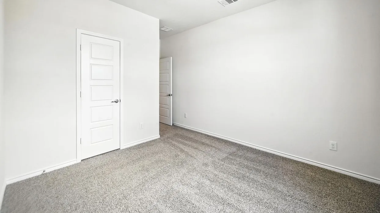 Spacious bedroom featuring neutral wall finishes, neutral carpet flooring, and a white six-panel entry door with brushed nickel hardware