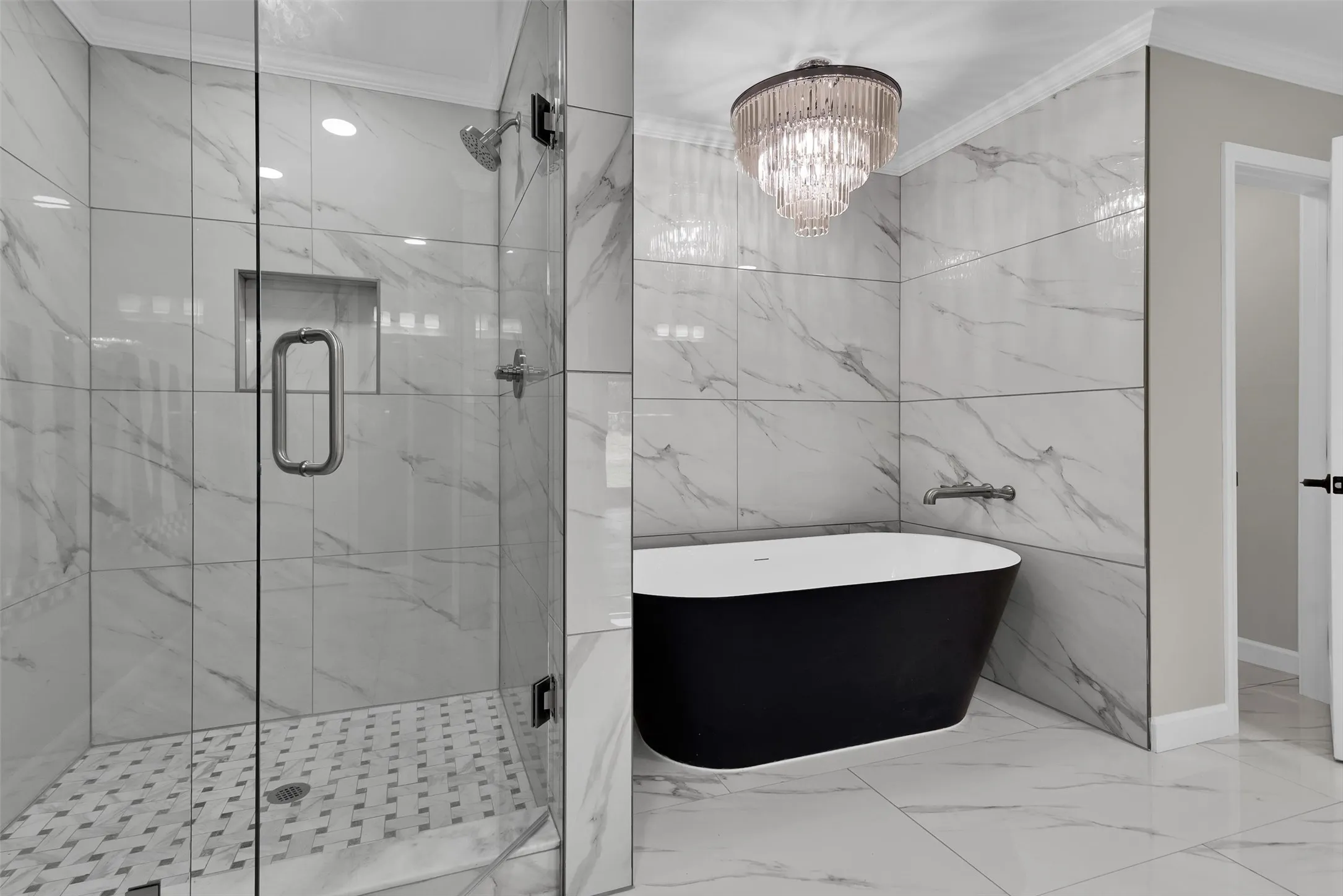 Freestanding black soaking tub, clear glass shower enclosure, shower niche, and ceiling-mounted chandelier