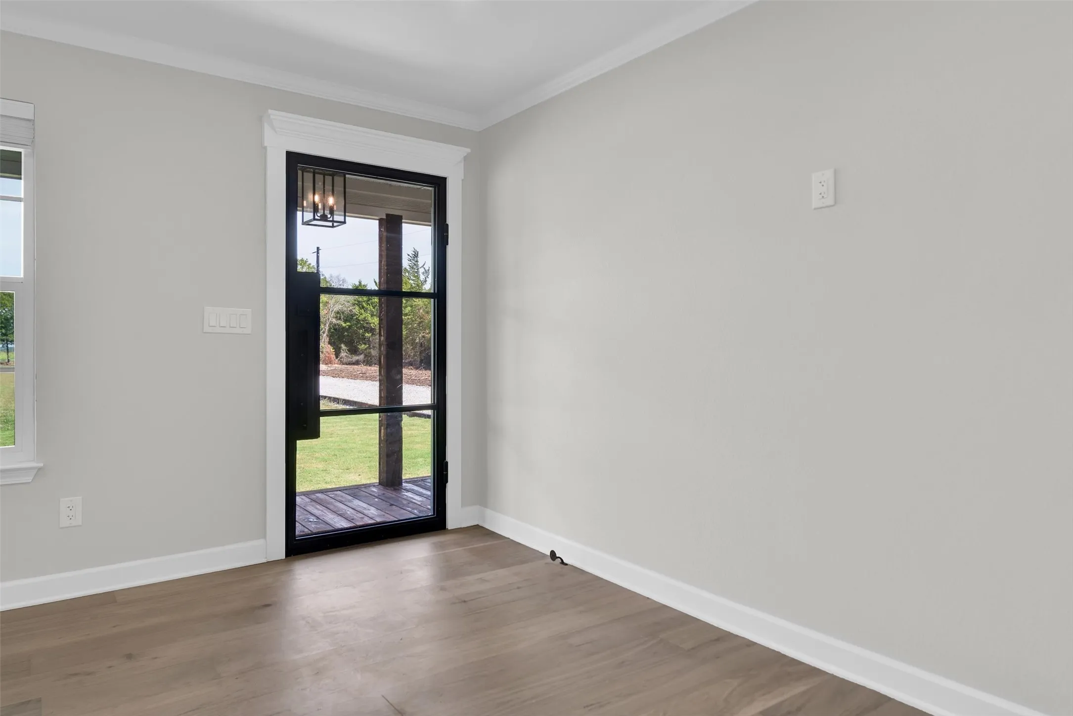 Black-framed glass entry door with transom detail, light-toned wood-finish flooring, and crown molding