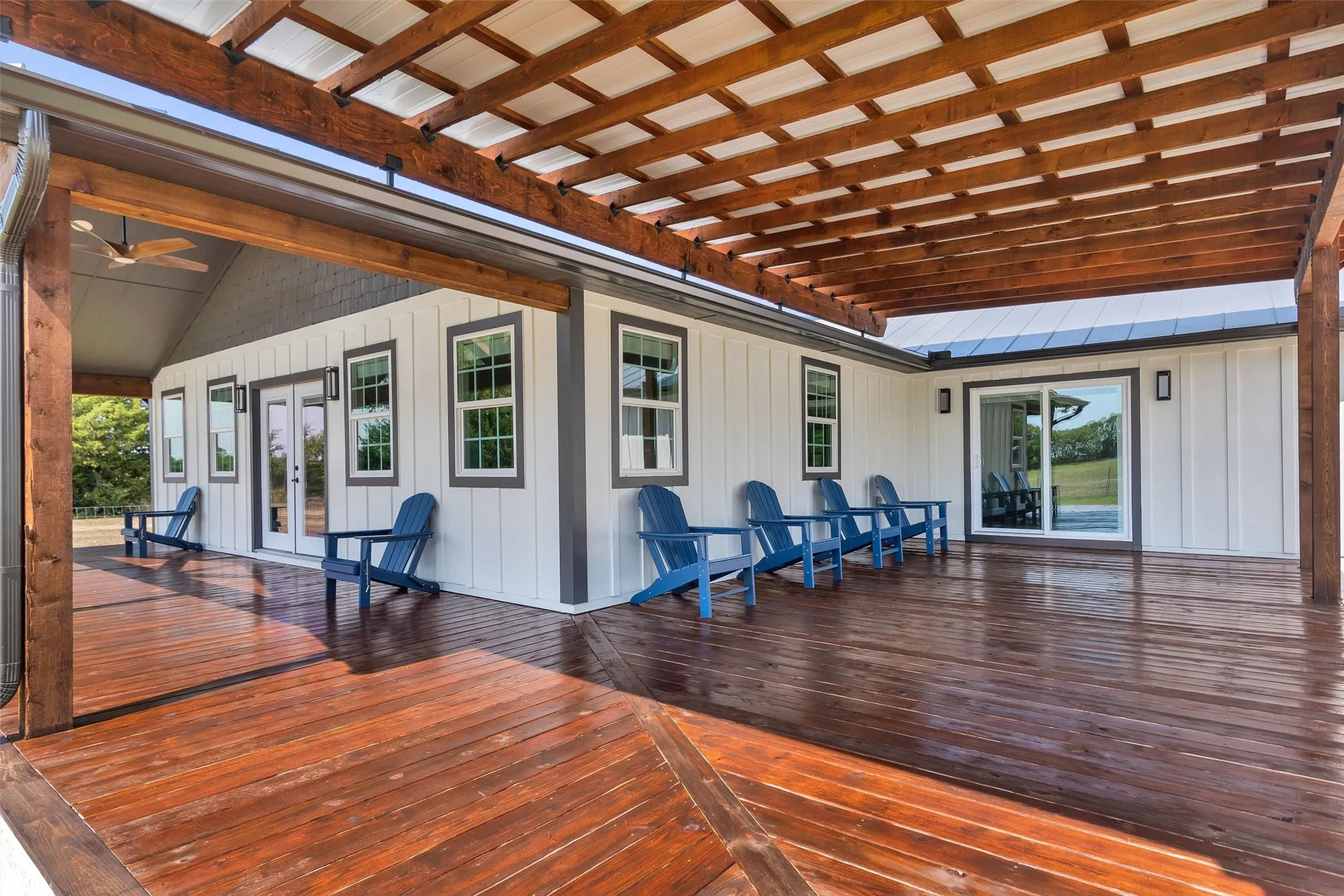 Expansive wood-finish deck with a wood pergola, white vertical siding, multiple windows, and a sliding glass door