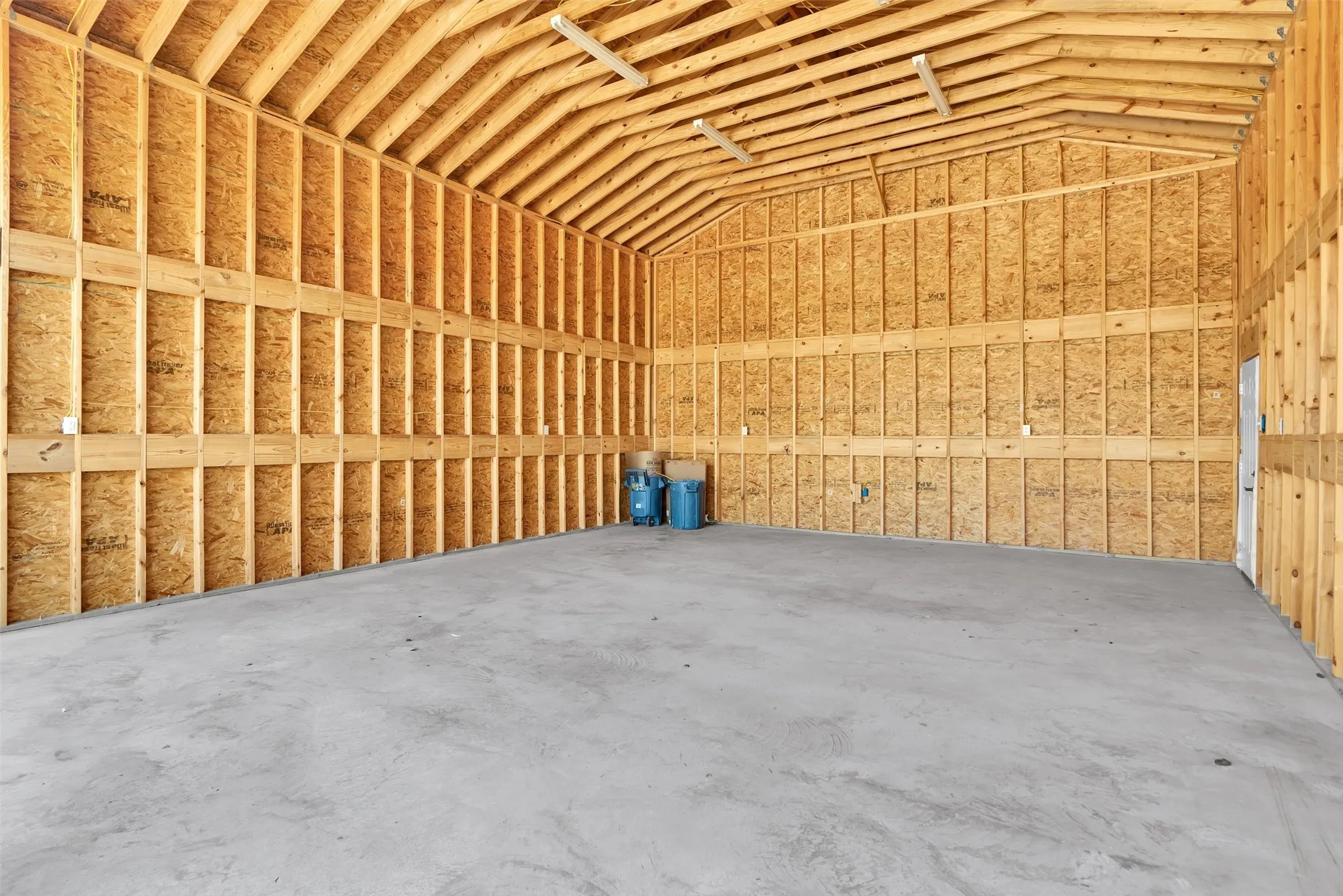 Vaulted wood-frame ceiling with exposed beams, concrete flooring, and unfinished wood-paneled walls