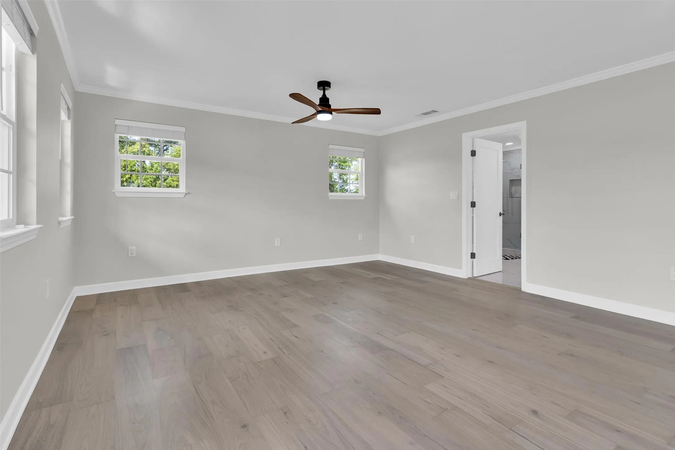 Wood-finish flooring throughout, bright walls, multiple windows with white trim, and a ceiling fan with integrated lighting