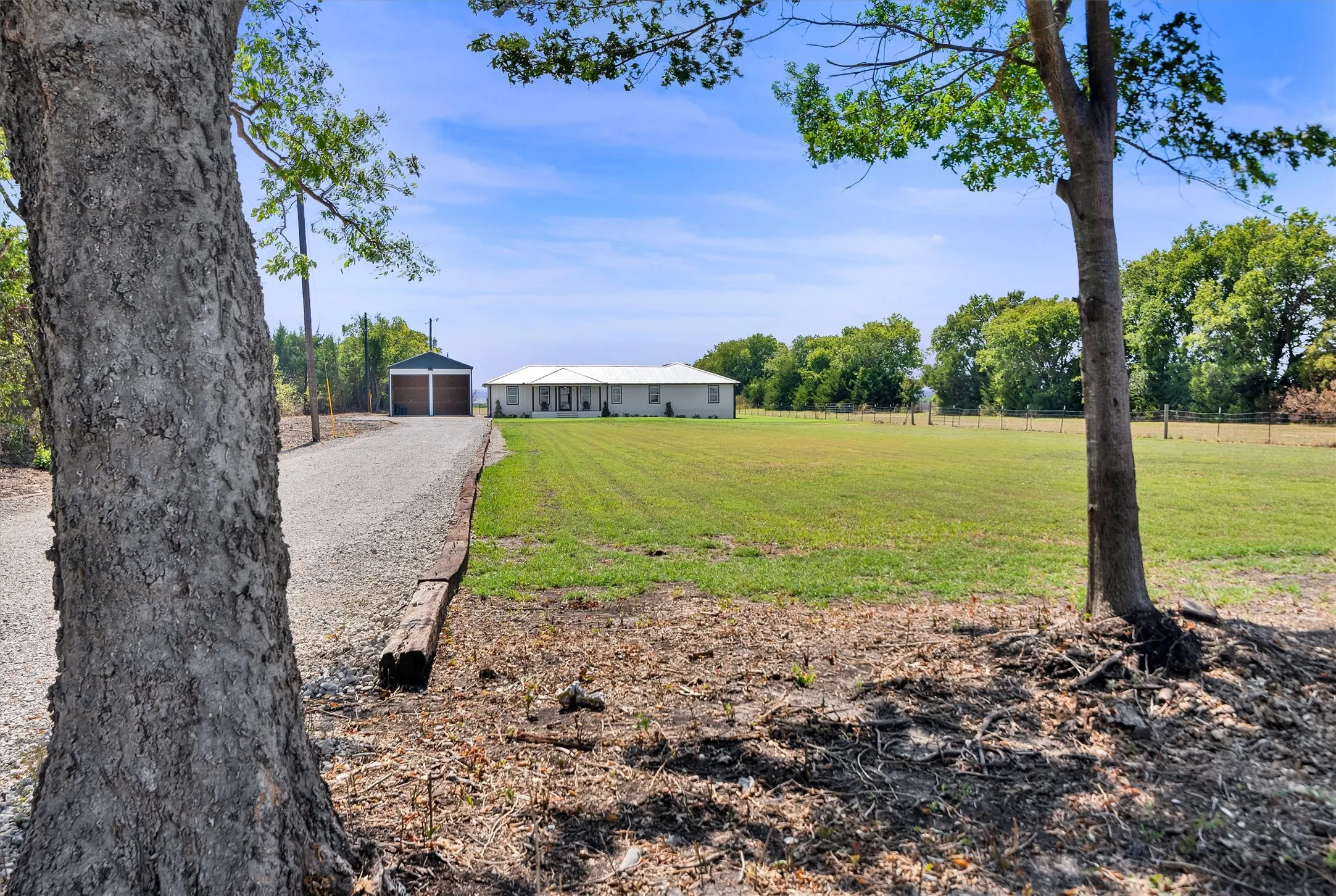 Expansive gravel driveway leading to a detached two-car garage with wood-finish doors