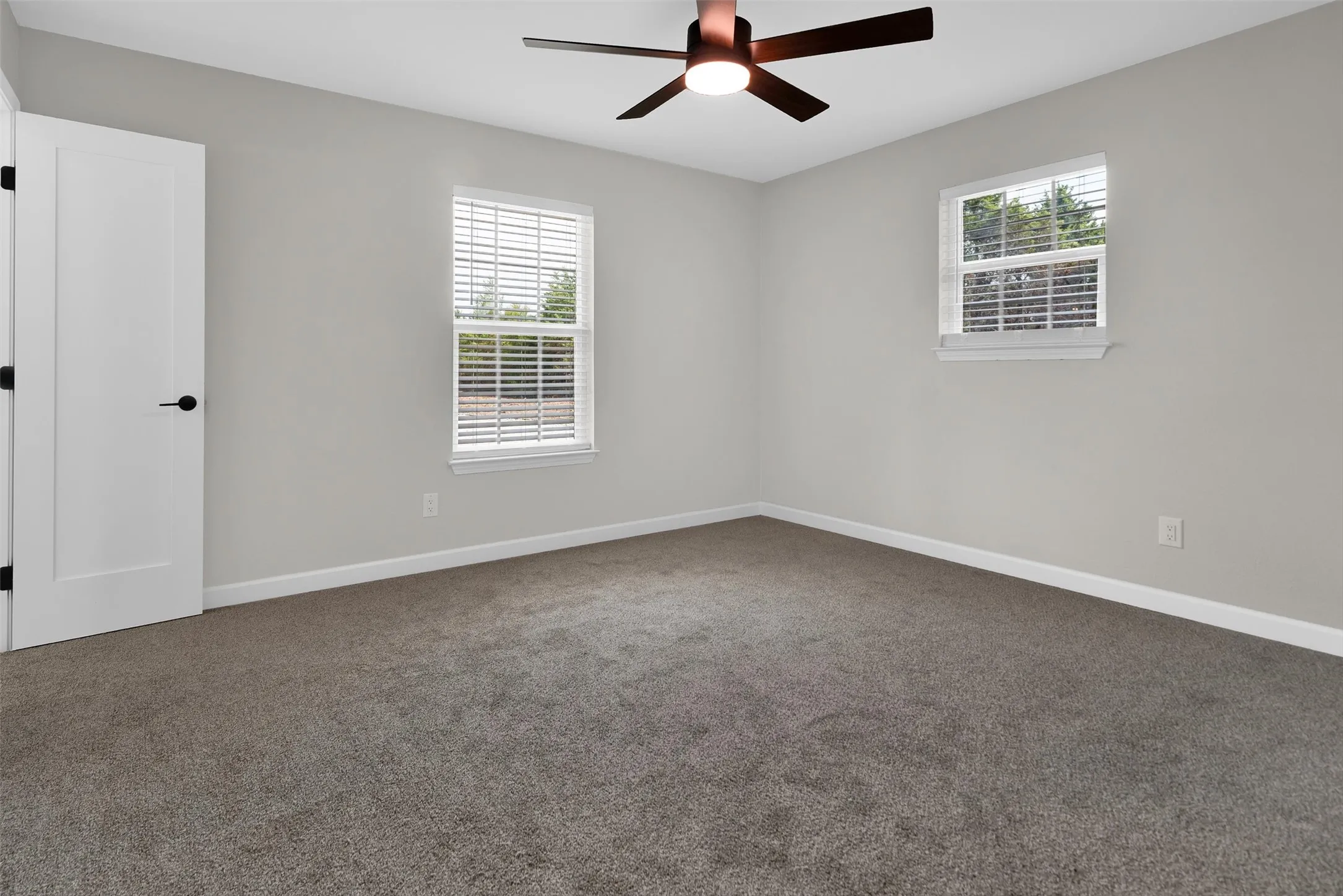 Neutral wall paint, gray carpeting, dual windows with blinds, a white interior door, and a ceiling fan with integrated lighting