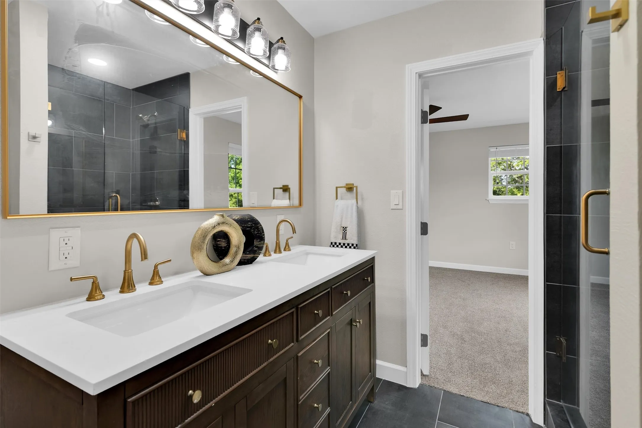 Dual sink vanity with white countertop, brass fixtures, and a large framed mirror