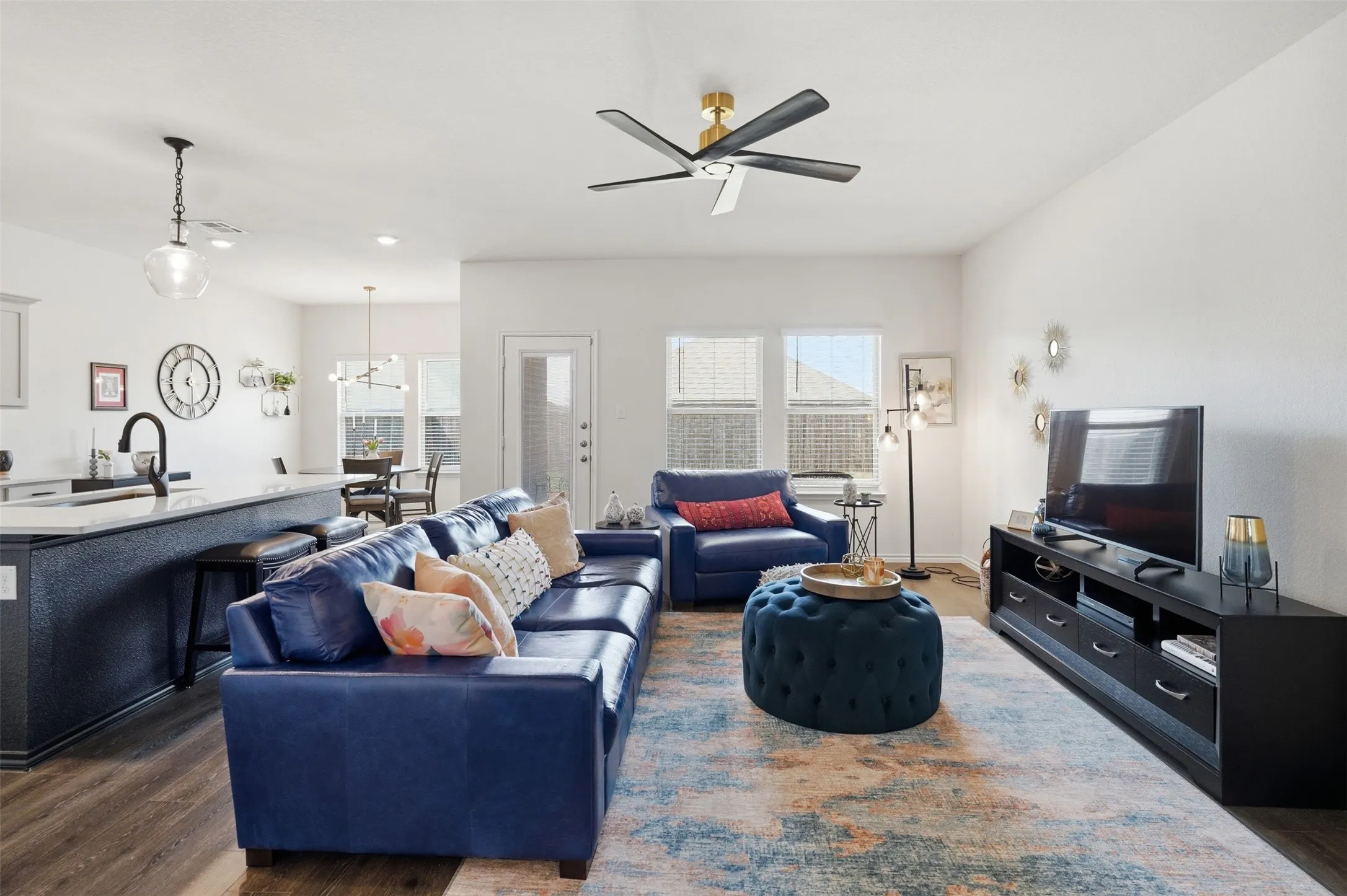 Living Room - Open-concept living area with wood-finish flooring, a modern ceiling fan, and multiple windows