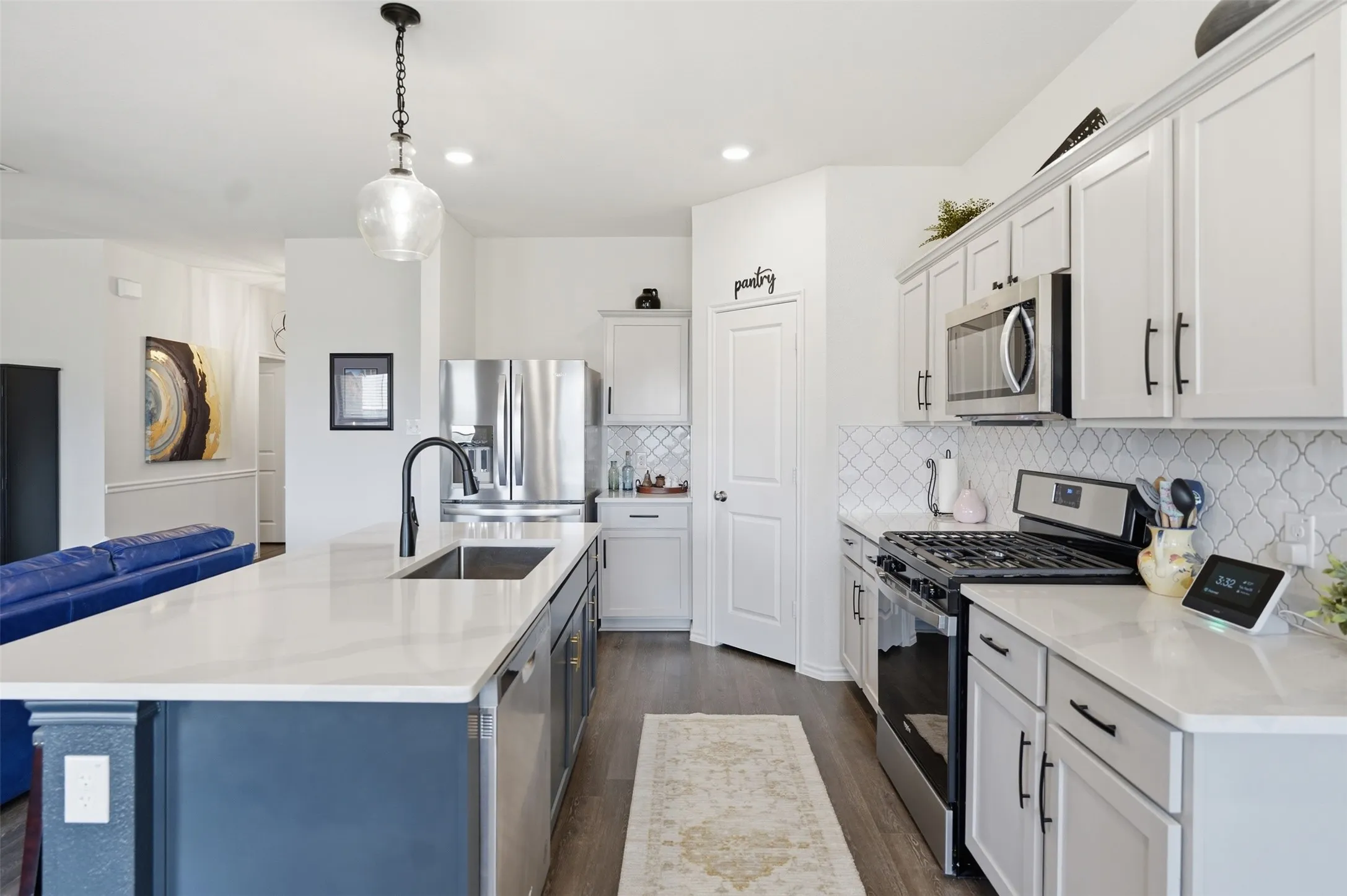 Kitchen featuring a large island with sink, white shaker cabinetry, stainless steel appliances, and wood-finish flooring