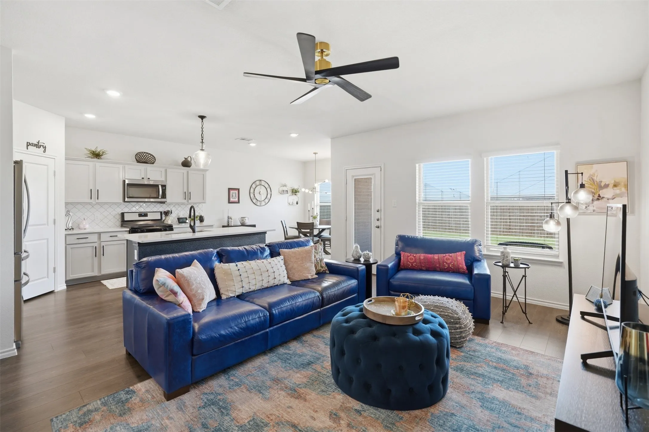Open-concept living space featuring wood-finish flooring, a contemporary ceiling fan, and multiple windows