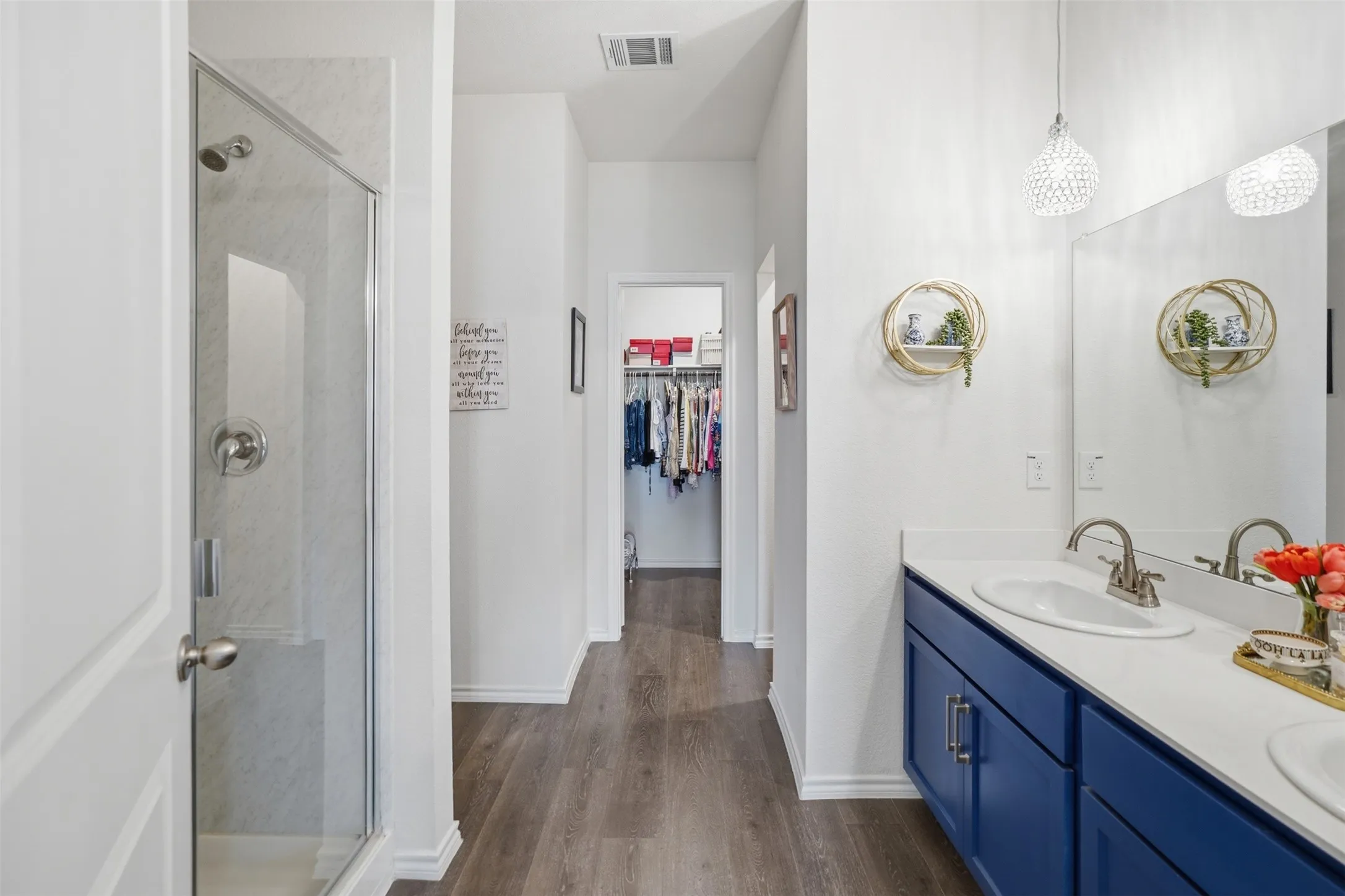 Walk-in shower with clear glass enclosure, a double vanity with an integrated countertop, wood-finish flooring, and pendant lighting