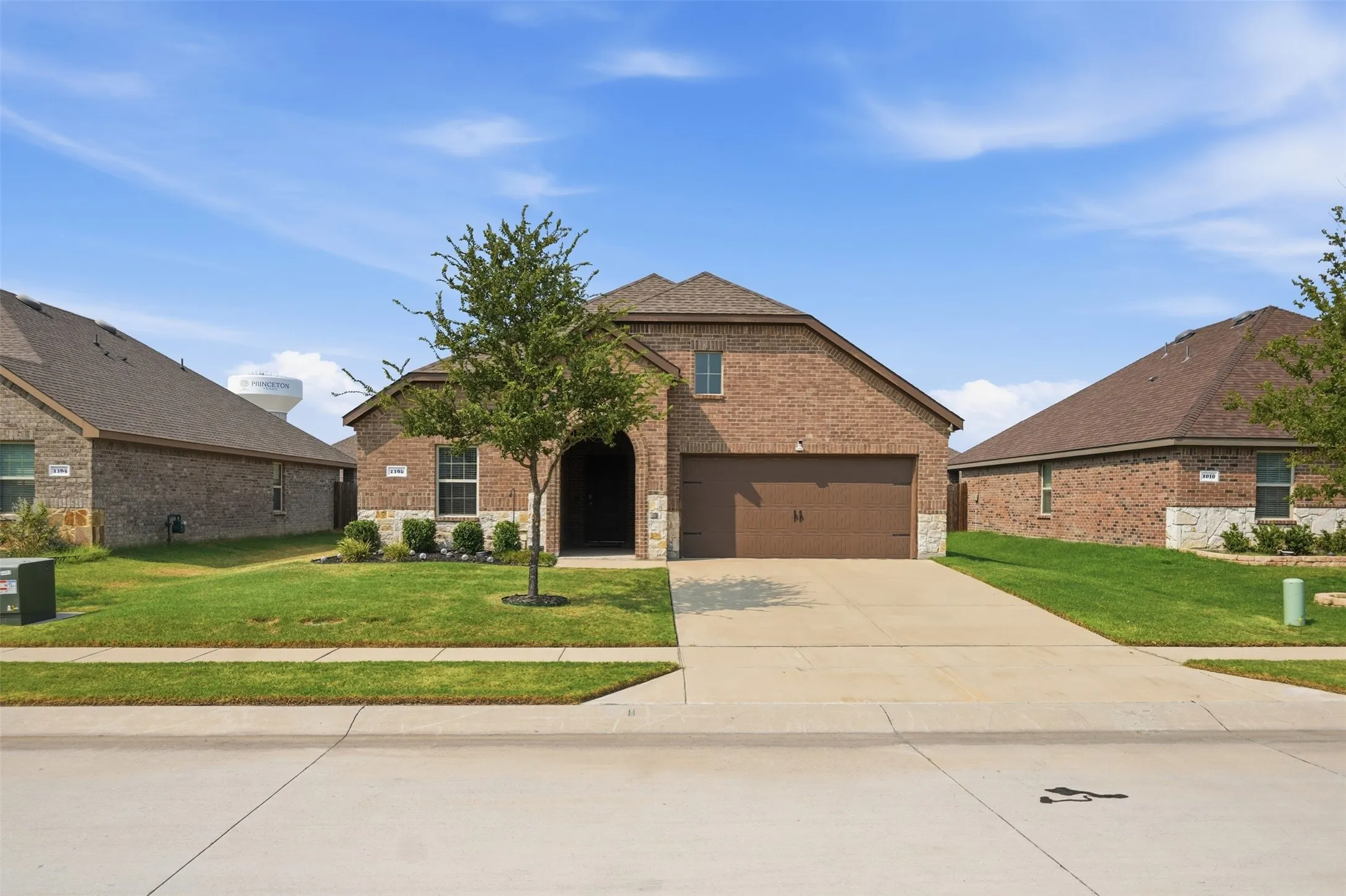 Brick and stone veneer exterior with an arched entryway, attached two-car garage, concrete driveway, and established front landscaping
